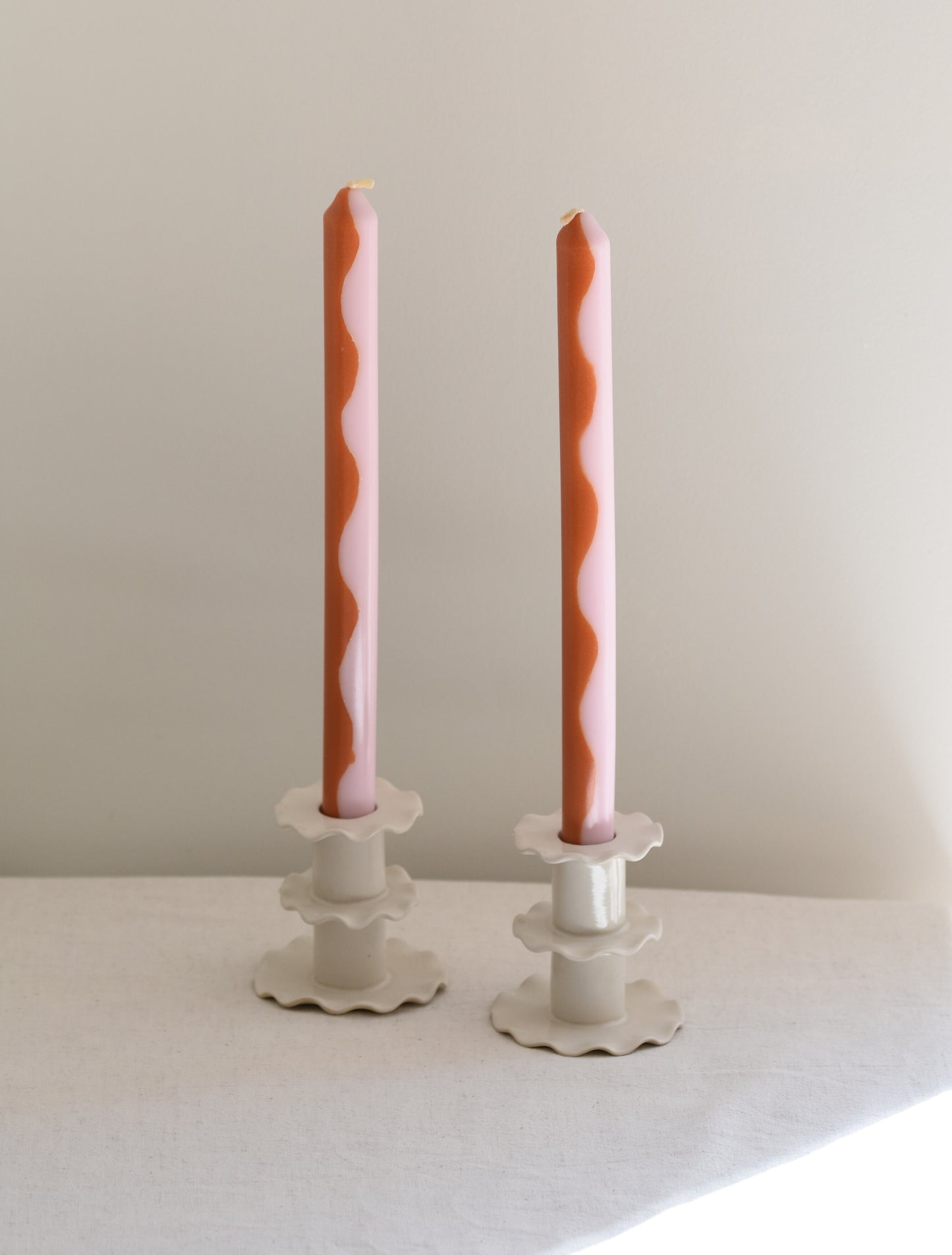A pair of two Pygmalion London Marmalade dinner candles with wave design in burnt orange and pale pink.