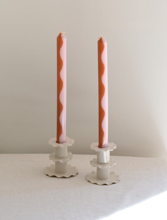 A pair of two Pygmalion London Marmalade dinner candles with wave design in burnt orange and pale pink.