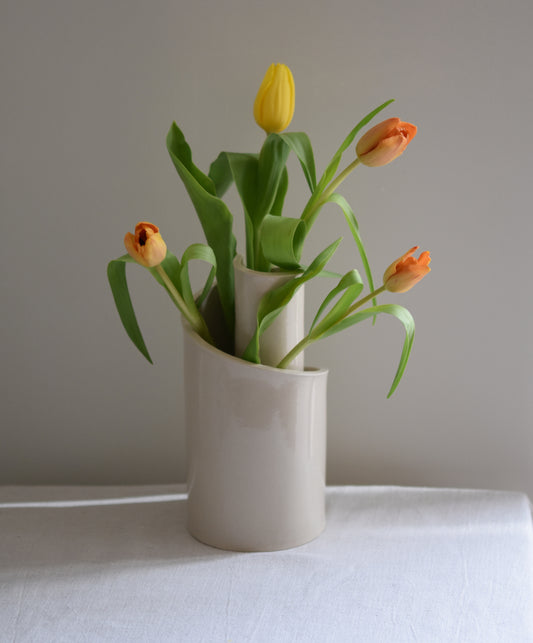 Brutes ceramics cream stoneware vase in a spiral shape with clear glossy finish, filled with orange and yellow tulips.