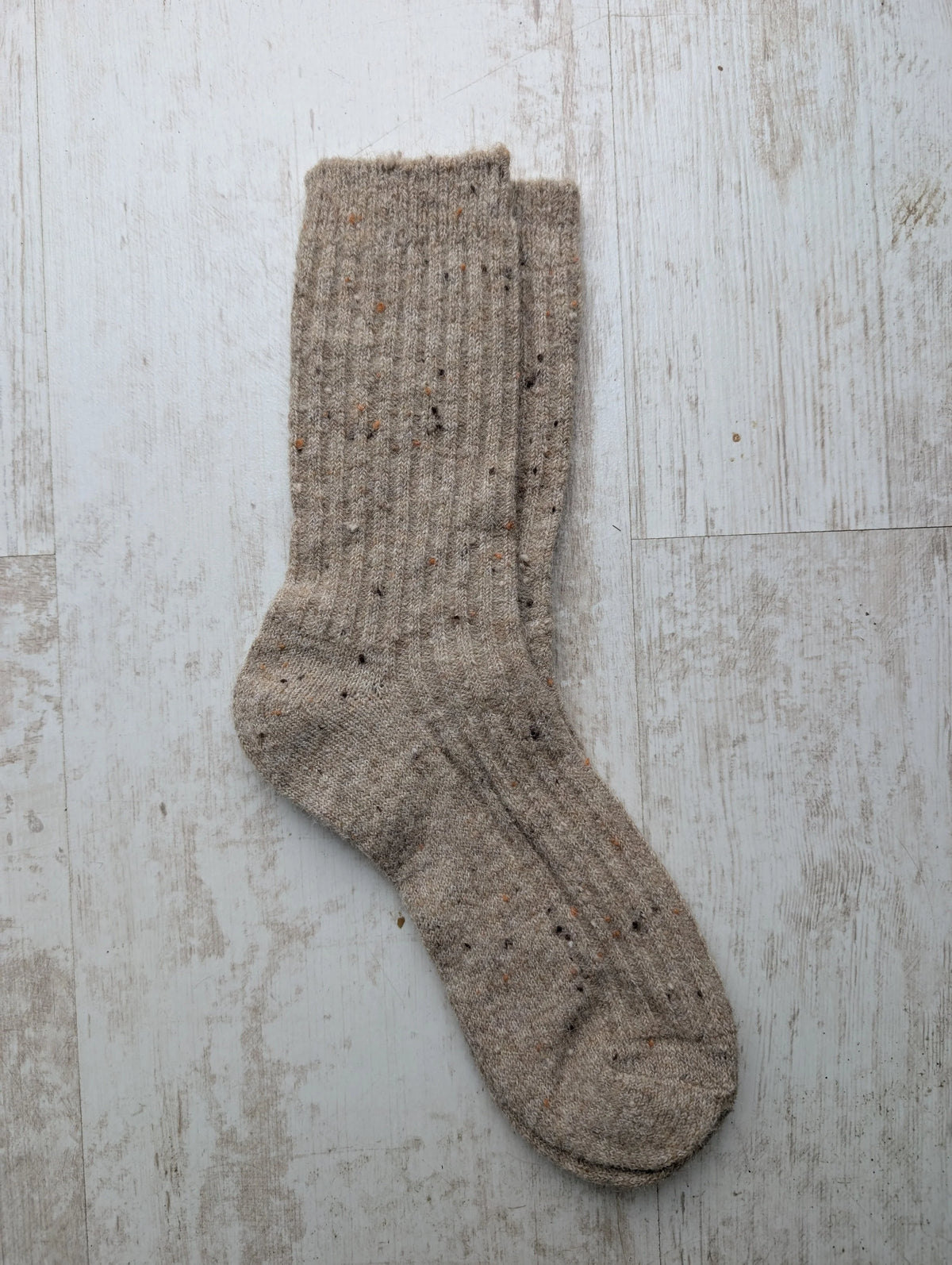 A pair of beige fleck ribbed knit Merino wool socks laid flat on a light wood surface.