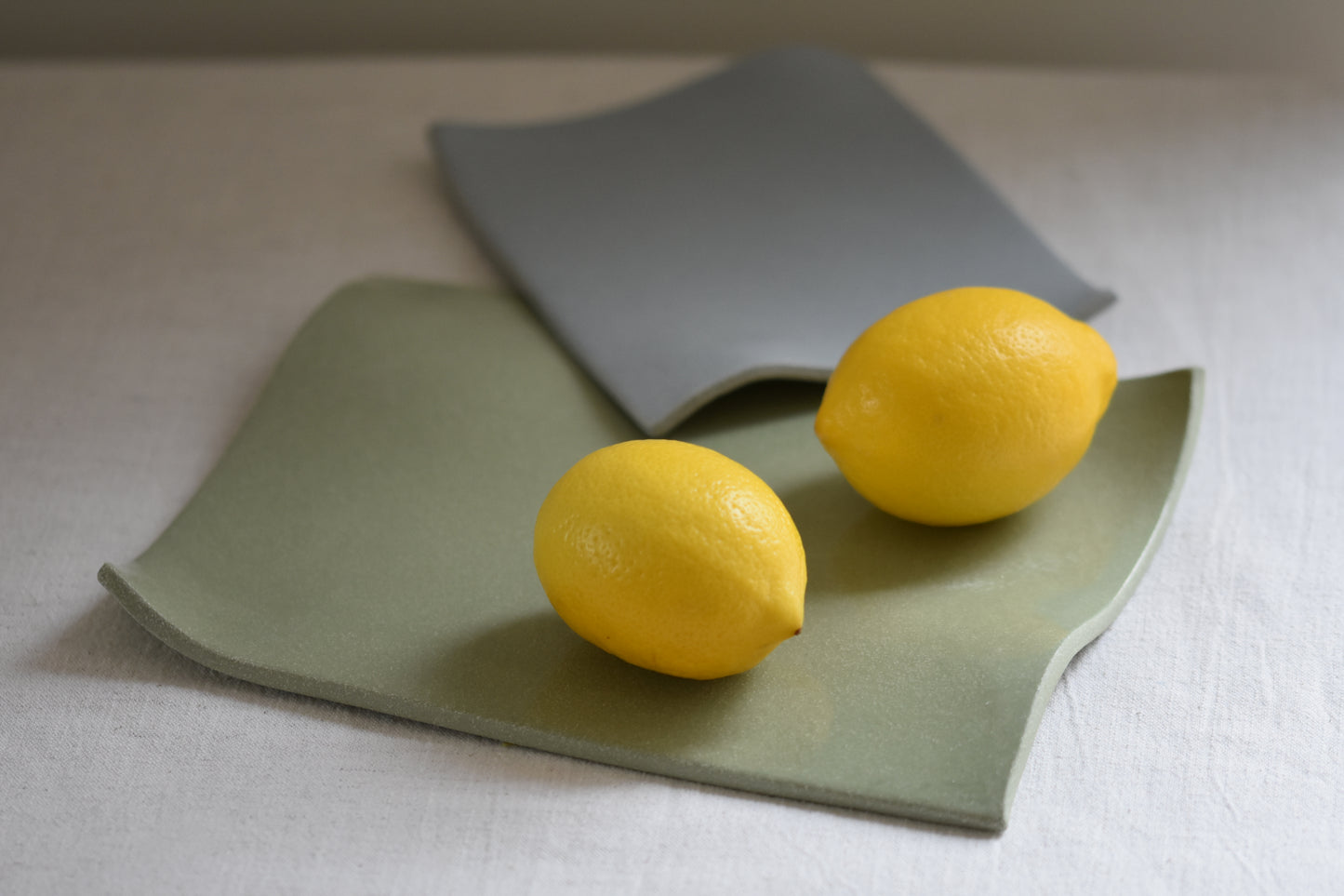 Brutes ceramics medium stoneware rumpled wavy platter in pistachio green with lemons and small stoneware rumpled wavy platter in pale blue.