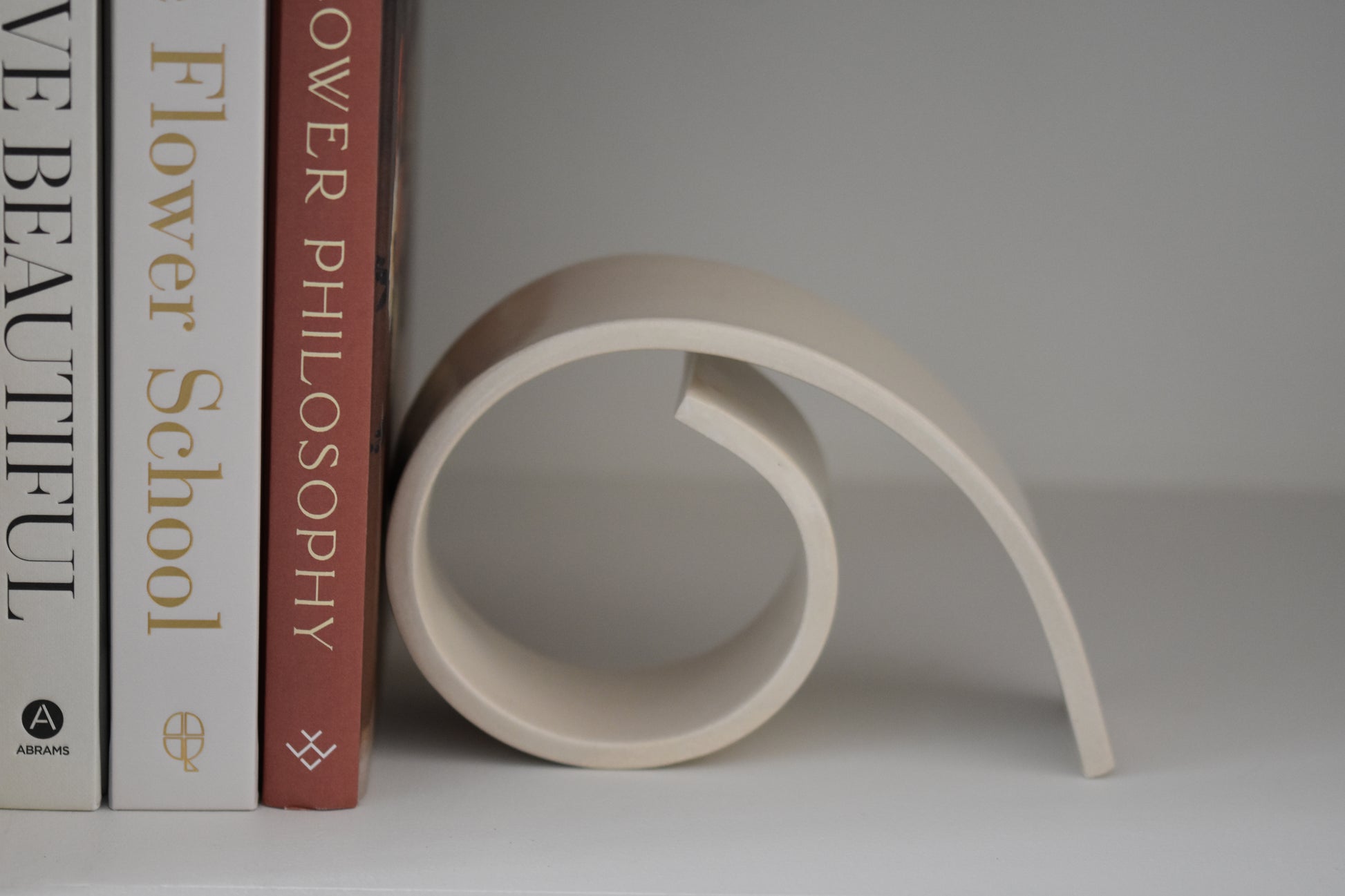 Brutes ceramics large spiral bookend in cream glossy stoneware holding up books on a shelf.