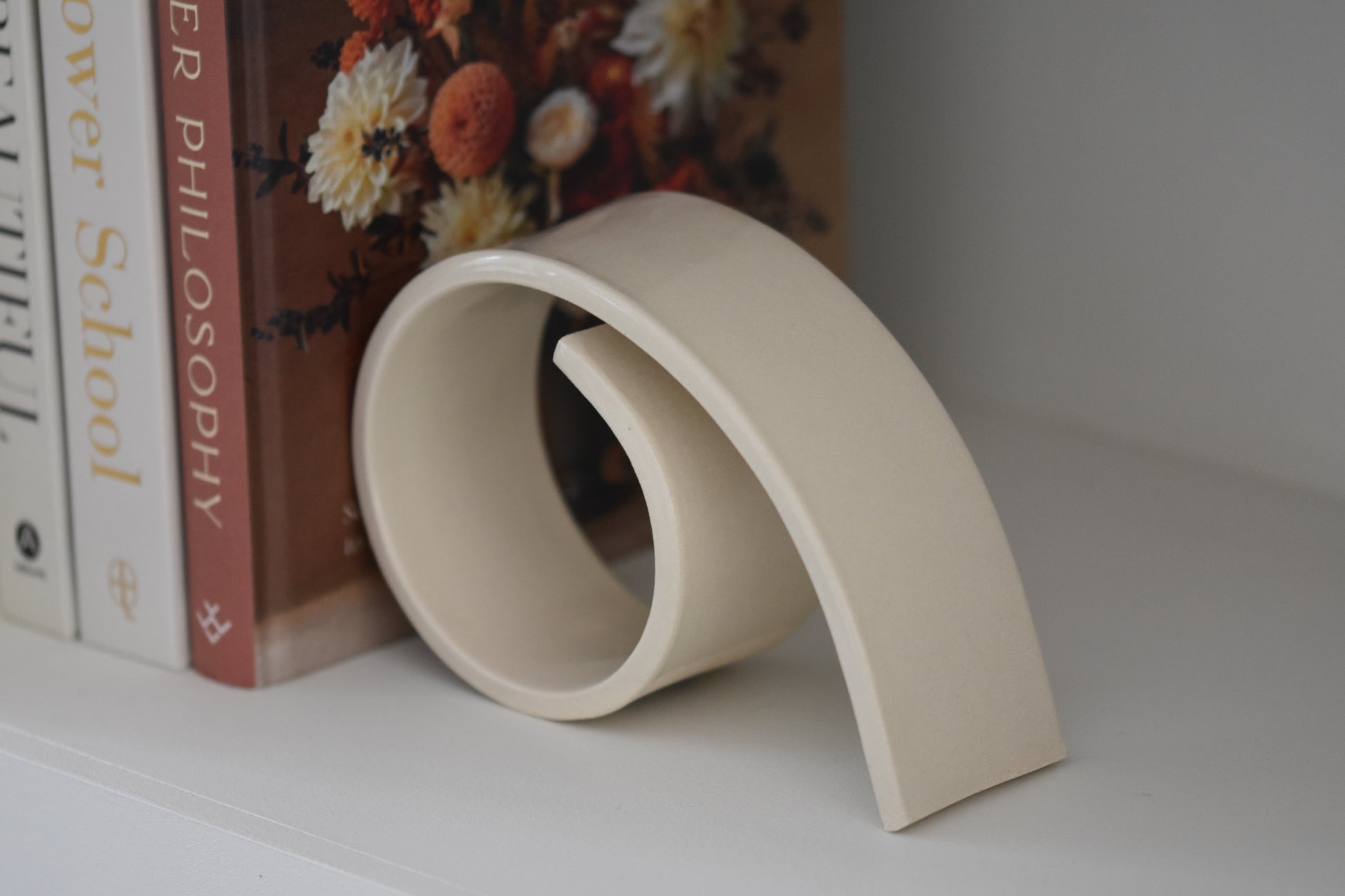 Brutes ceramics large spiral bookend in cream glossy stoneware holding up books on a shelf.