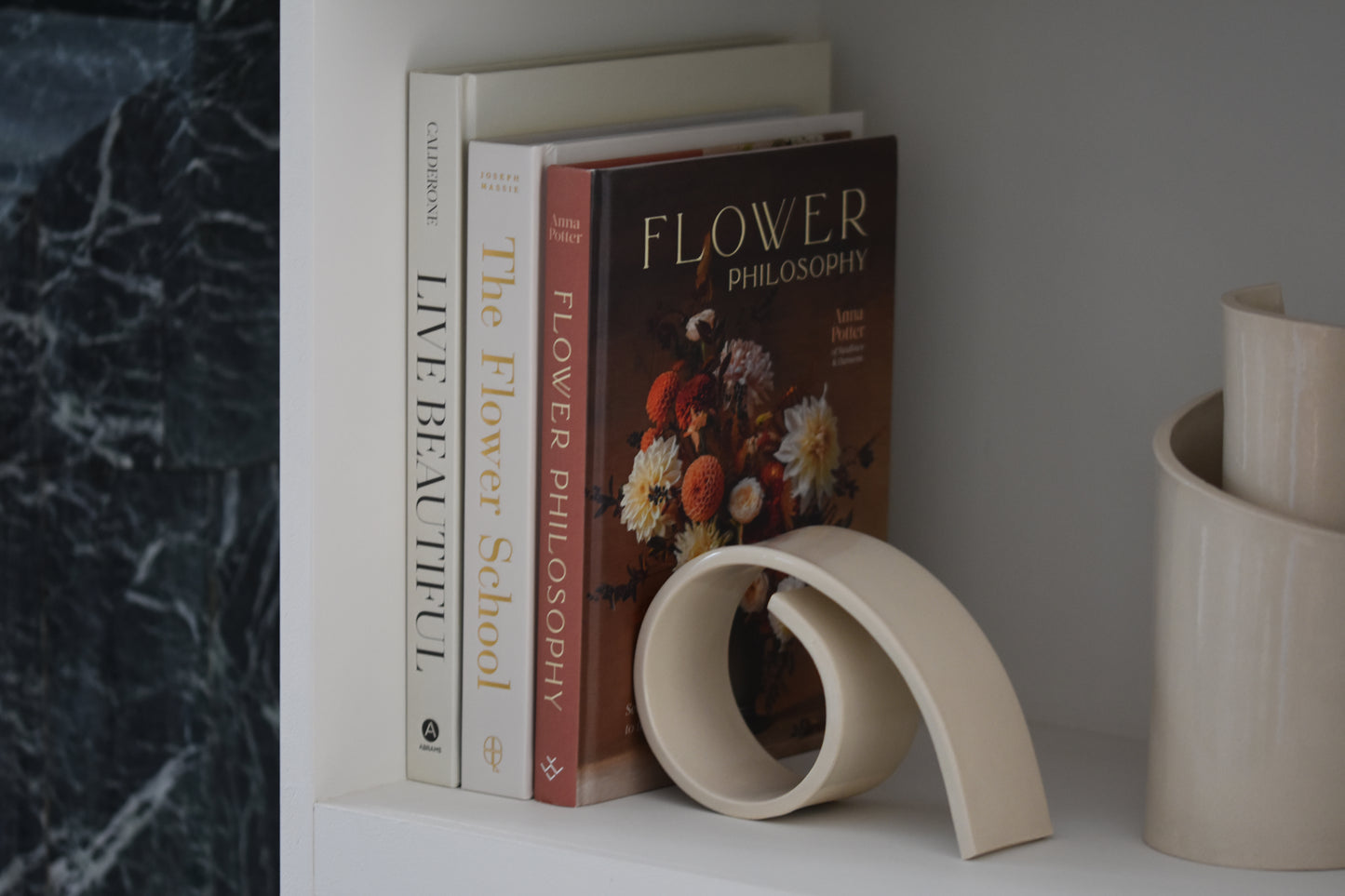 Brutes ceramics large spiral bookend in cream glossy stoneware holding up books on a shelf, with Brutes ceramics cream spiral vase.