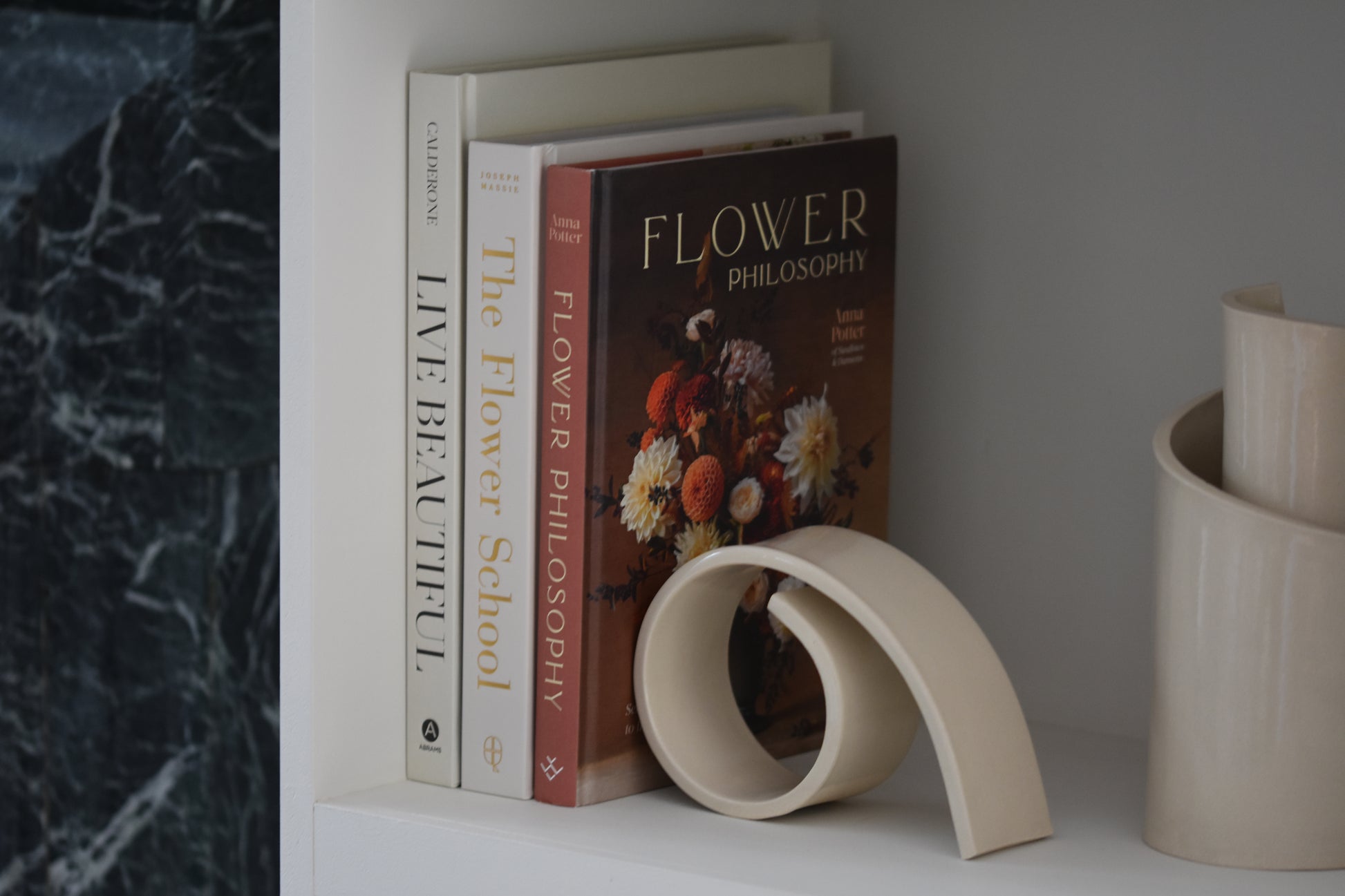 Brutes ceramics large spiral bookend in cream glossy stoneware holding up books on a shelf, with Brutes ceramics cream spiral vase.