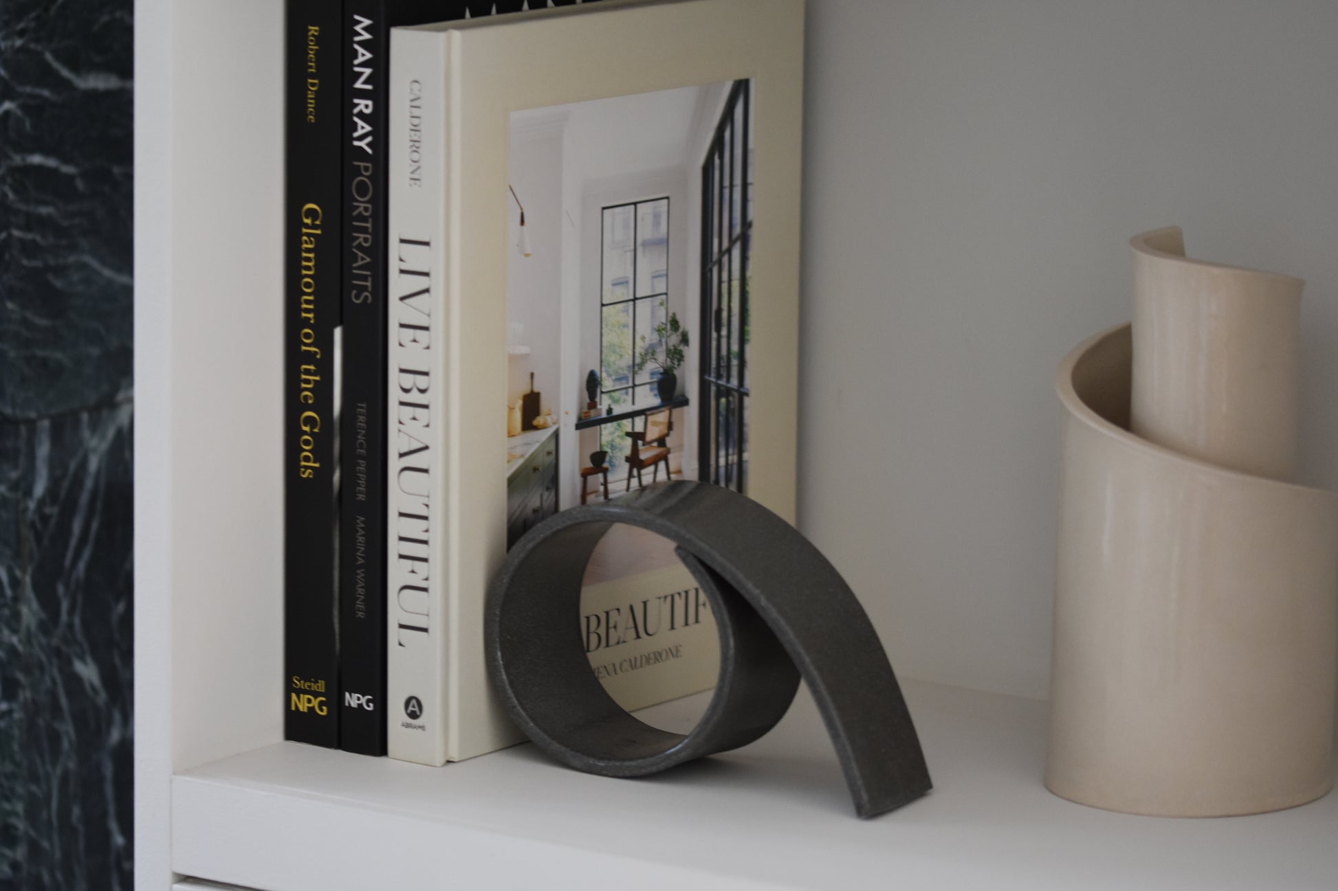 Brutes ceramics large spiral bookend in charcoal glossy stoneware holding up books on a shelf, with Brutes ceramics cream spiral vase.