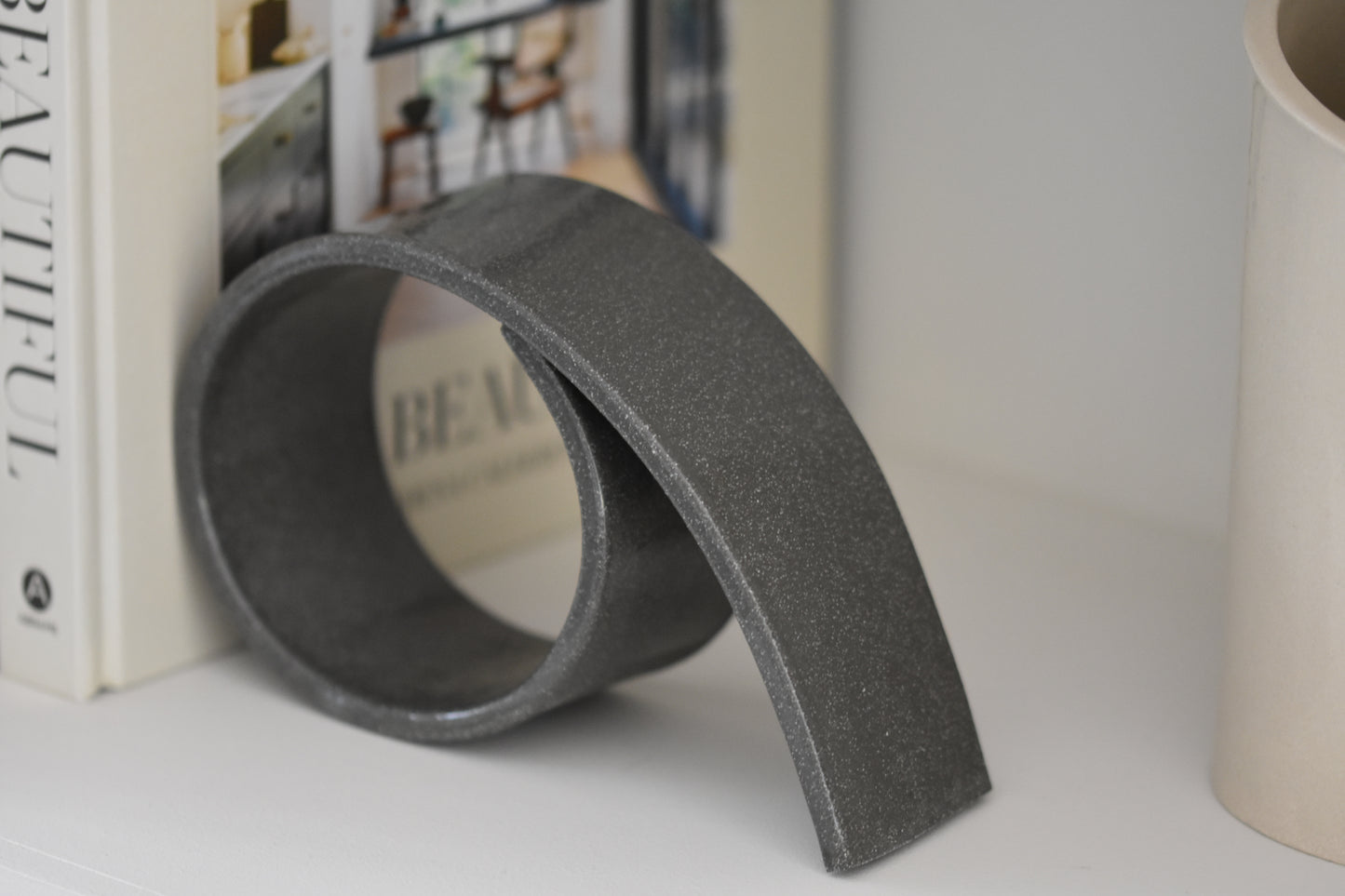Brutes ceramics large spiral bookend in charcoal glossy stoneware holding up books on a shelf.