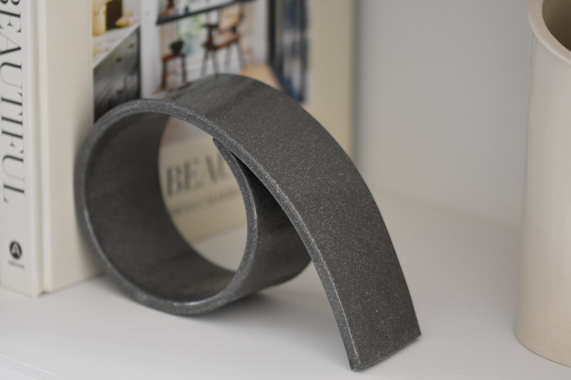 Brutes ceramics large spiral bookend in charcoal glossy stoneware holding up books on a shelf.