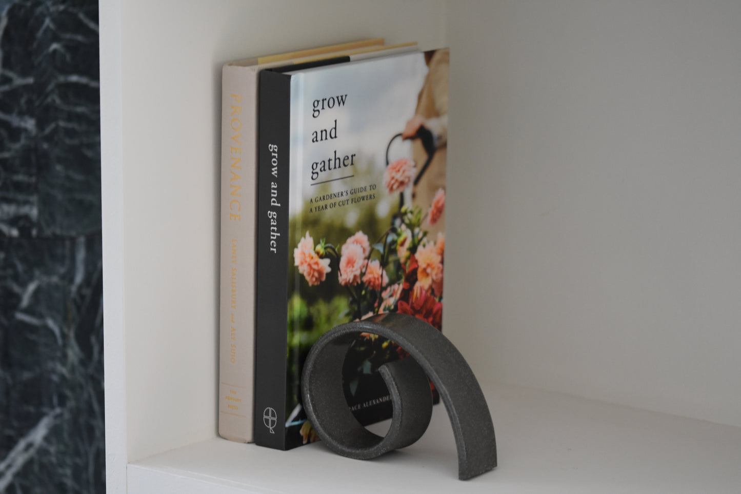 Brutes ceramics medium spiral bookend in charcoal glossy stoneware holding up books on a shelf.