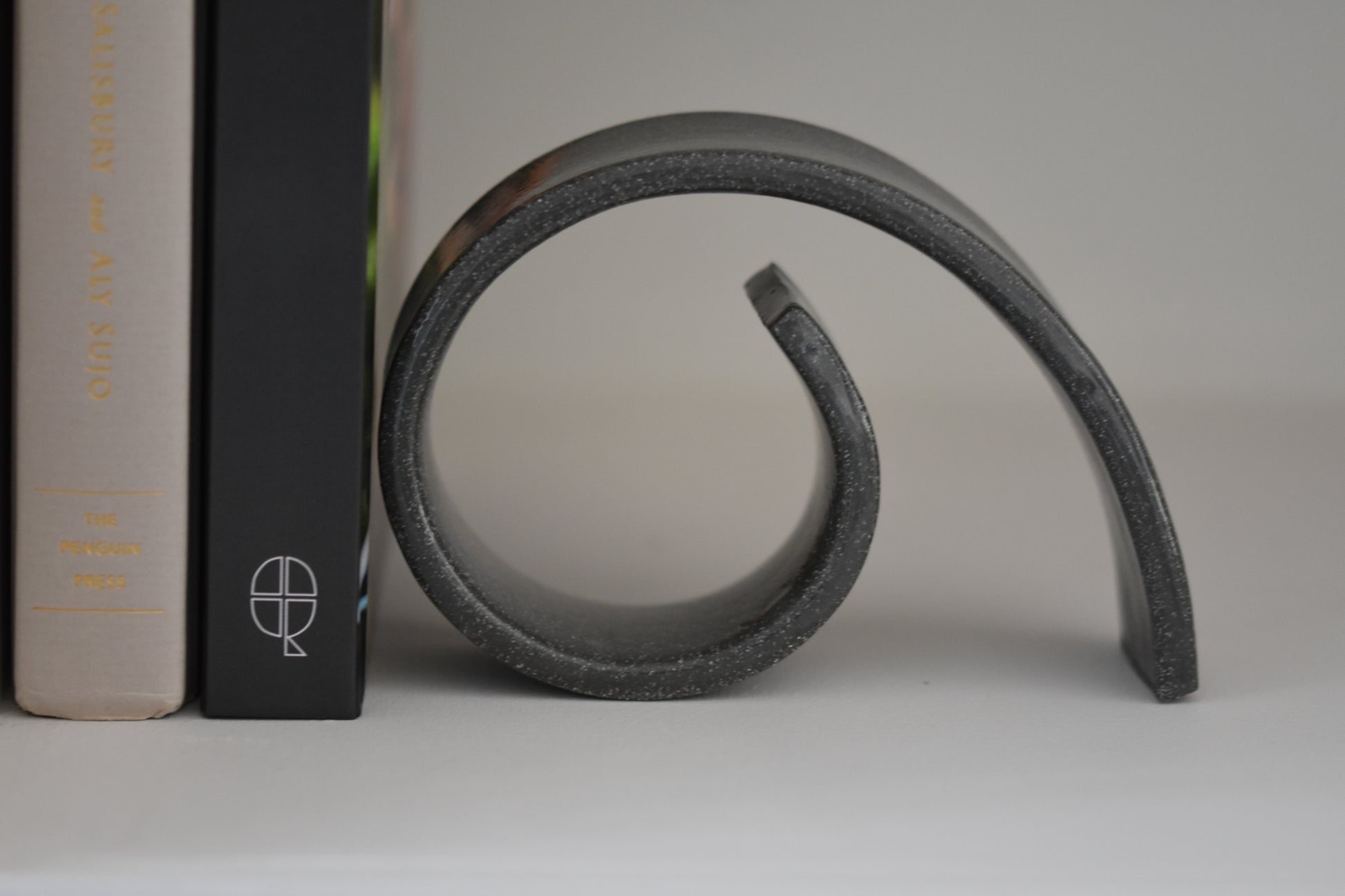 Brutes ceramics medium spiral bookend in charcoal glossy stoneware holding up books on a shelf.