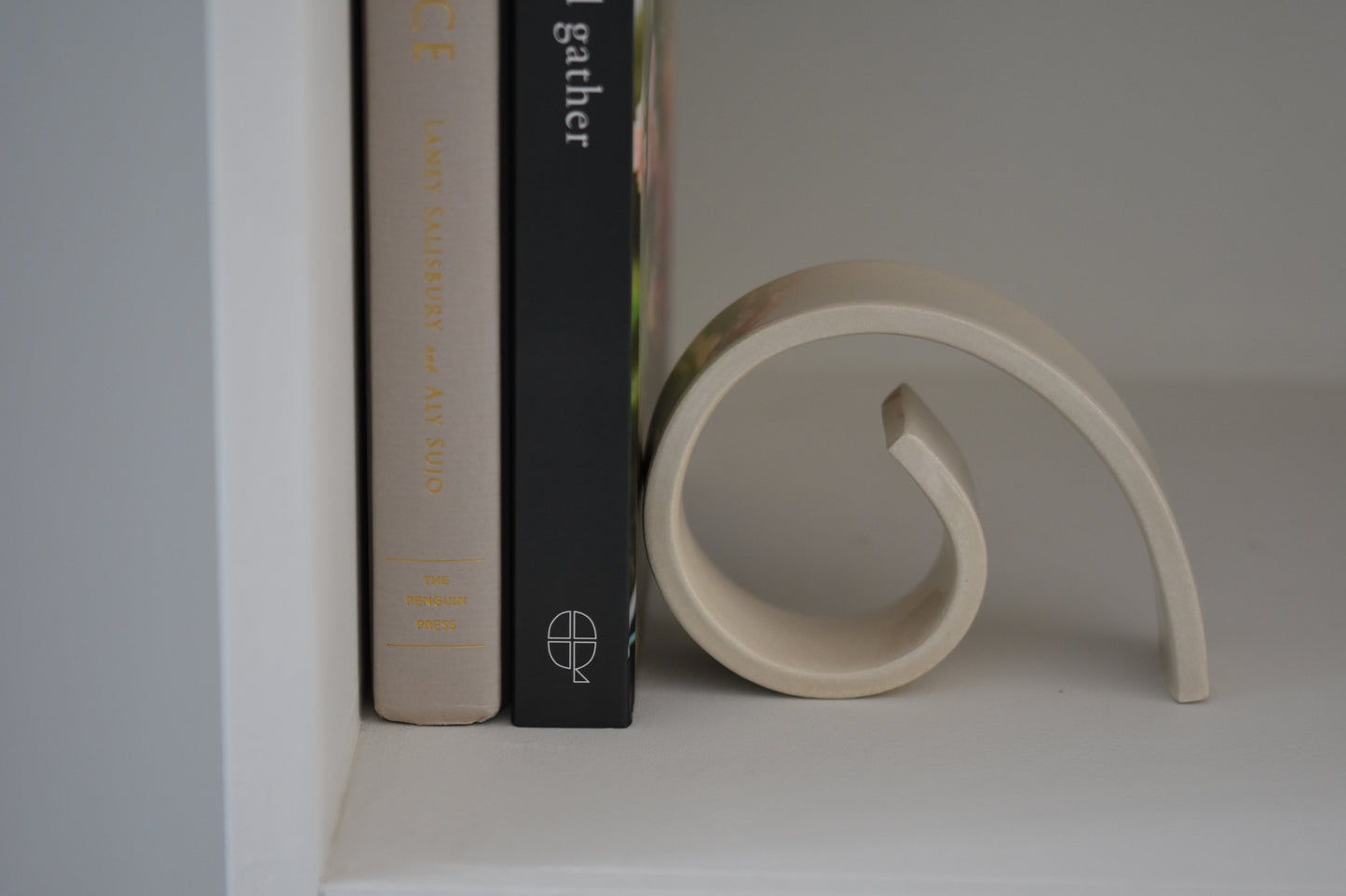 Brutes ceramics medium spiral bookend in cream glossy stoneware holding up books on a shelf.