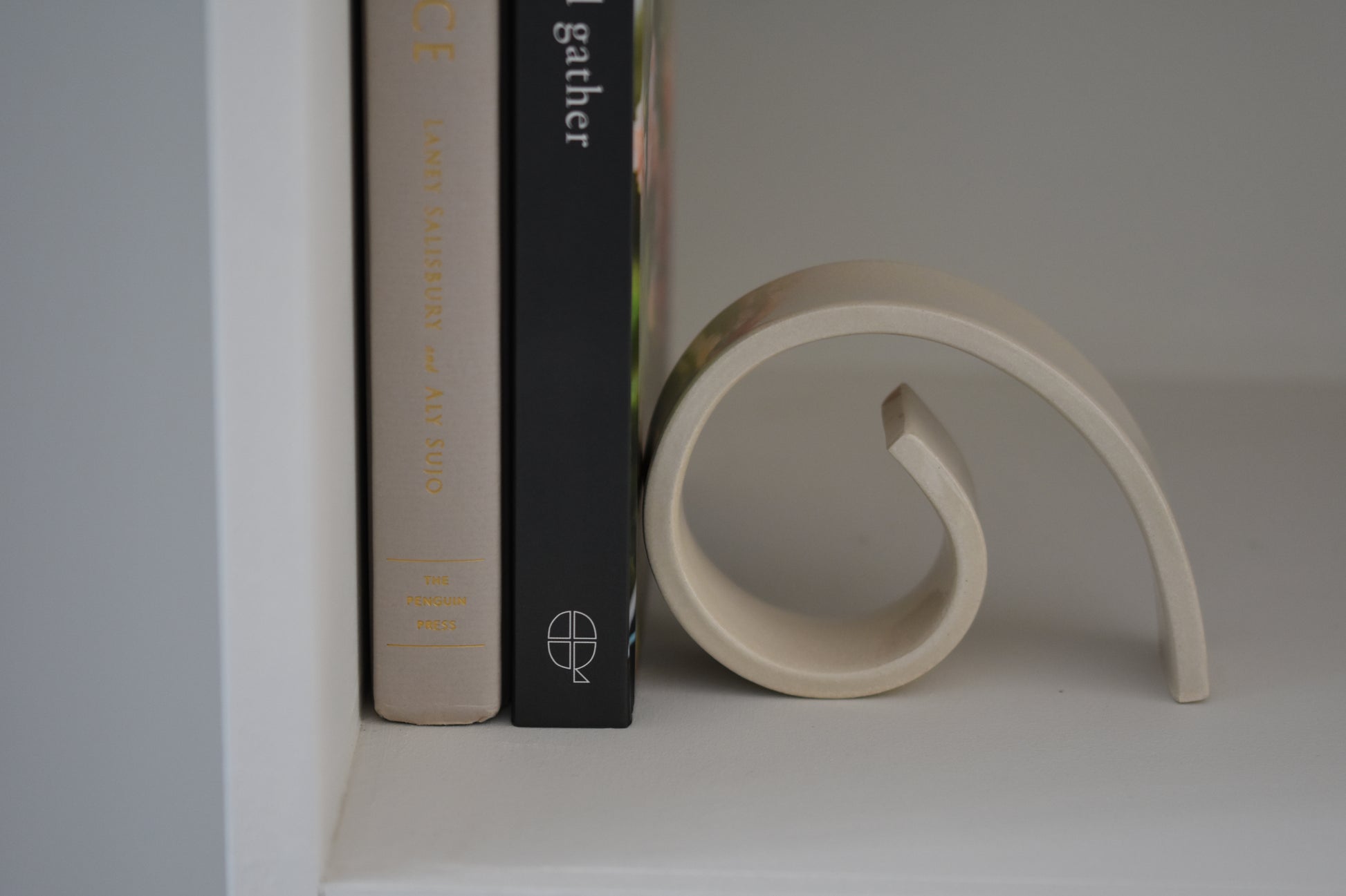 Brutes ceramics medium spiral bookend in cream glossy stoneware holding up books on a shelf.