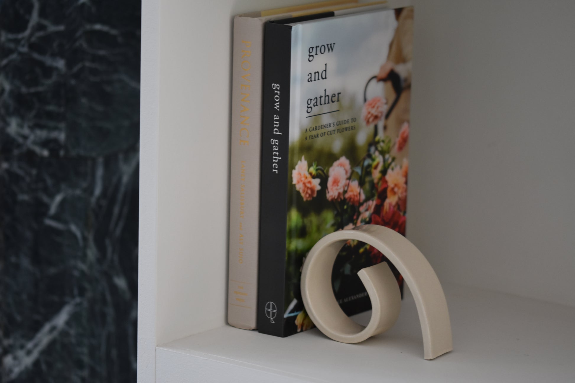 Brutes ceramics medium spiral bookend in cream glossy stoneware holding up books on a shelf.