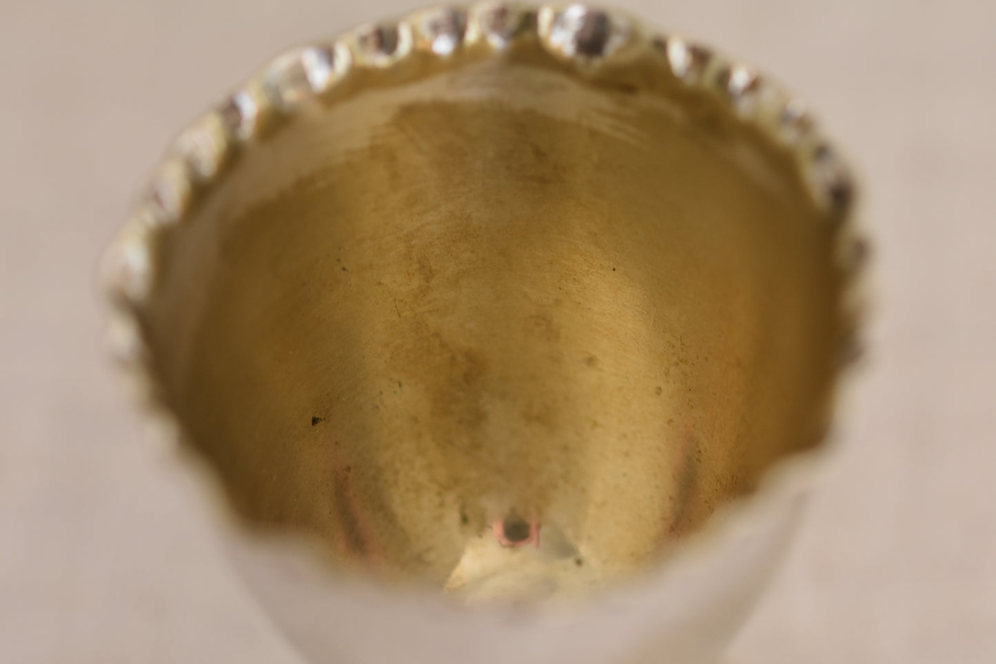 Close up of the inside of a vintage silver plated egg cup with crimped rim on a beige background.