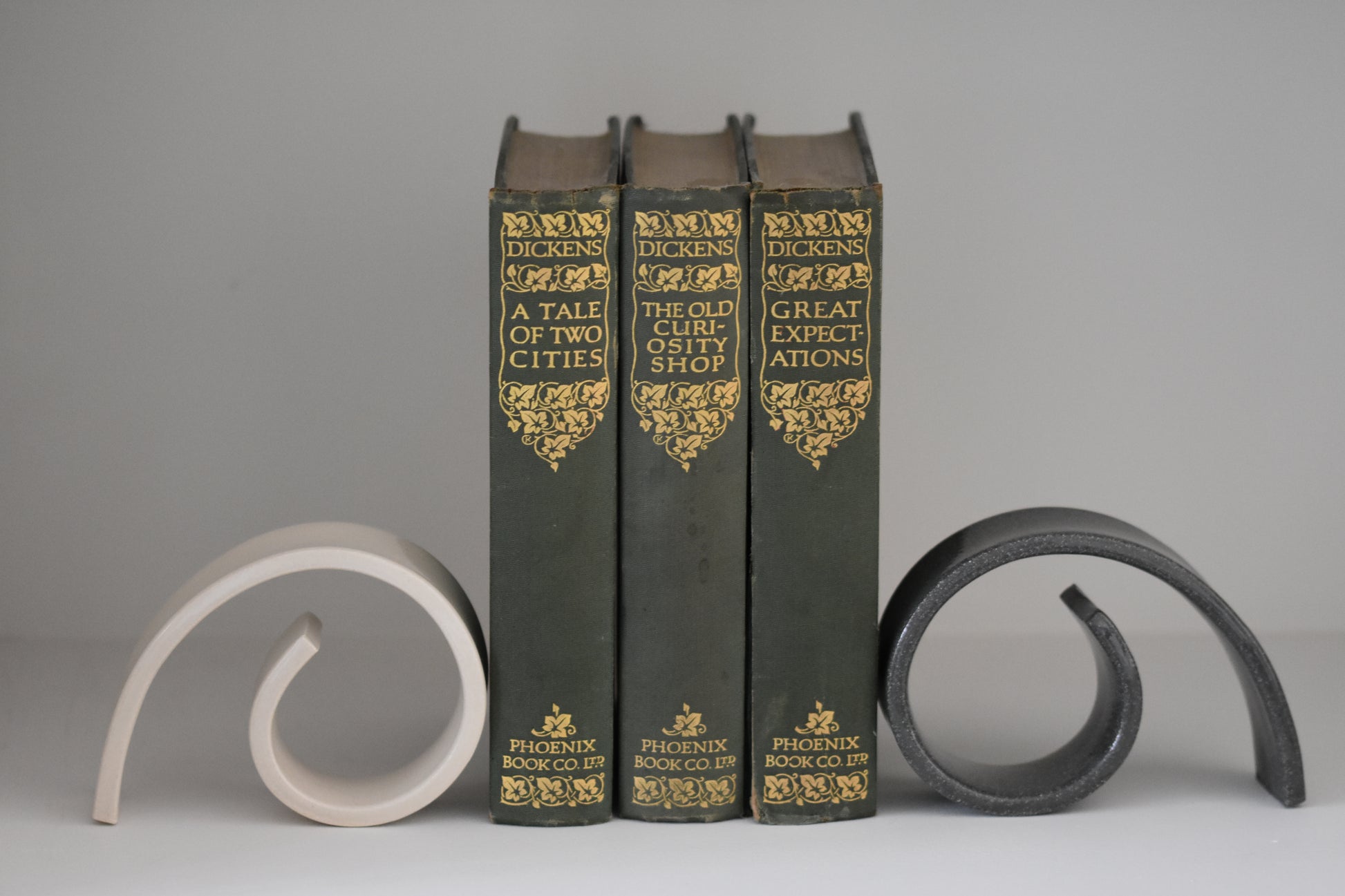 Brutes ceramics medium spiral bookends in charcoal and cream glossy stoneware holding up books on a shelf.