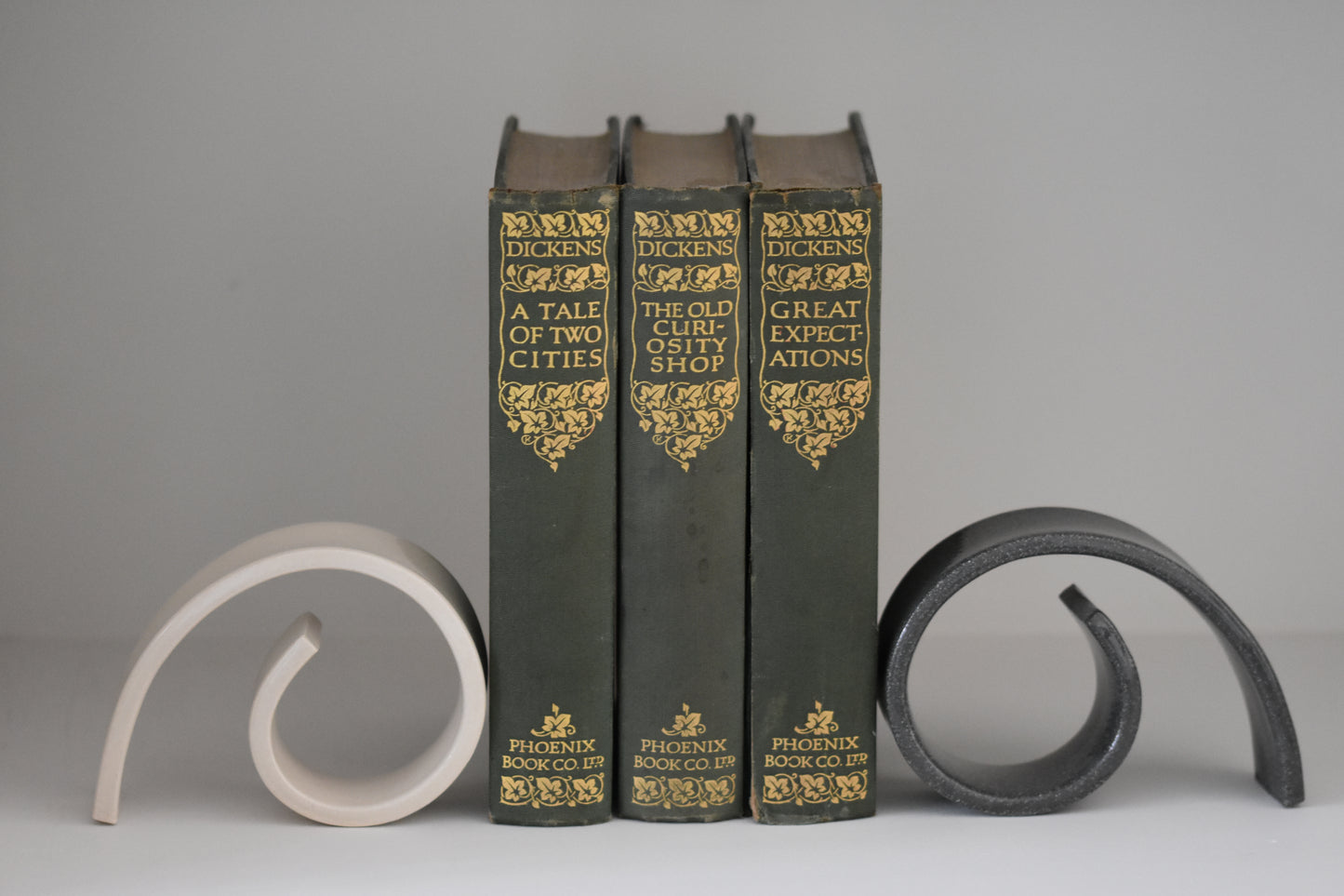 Brutes ceramics medium spiral bookends in charcoal and cream glossy stoneware holding up books on a shelf.