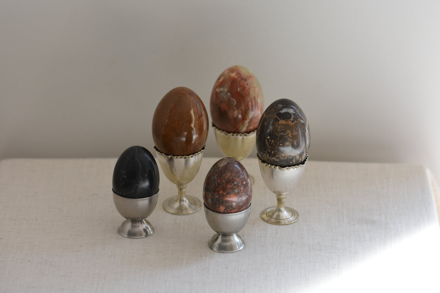 Silver egg cups containing five vintage stone eggs on a beige background.