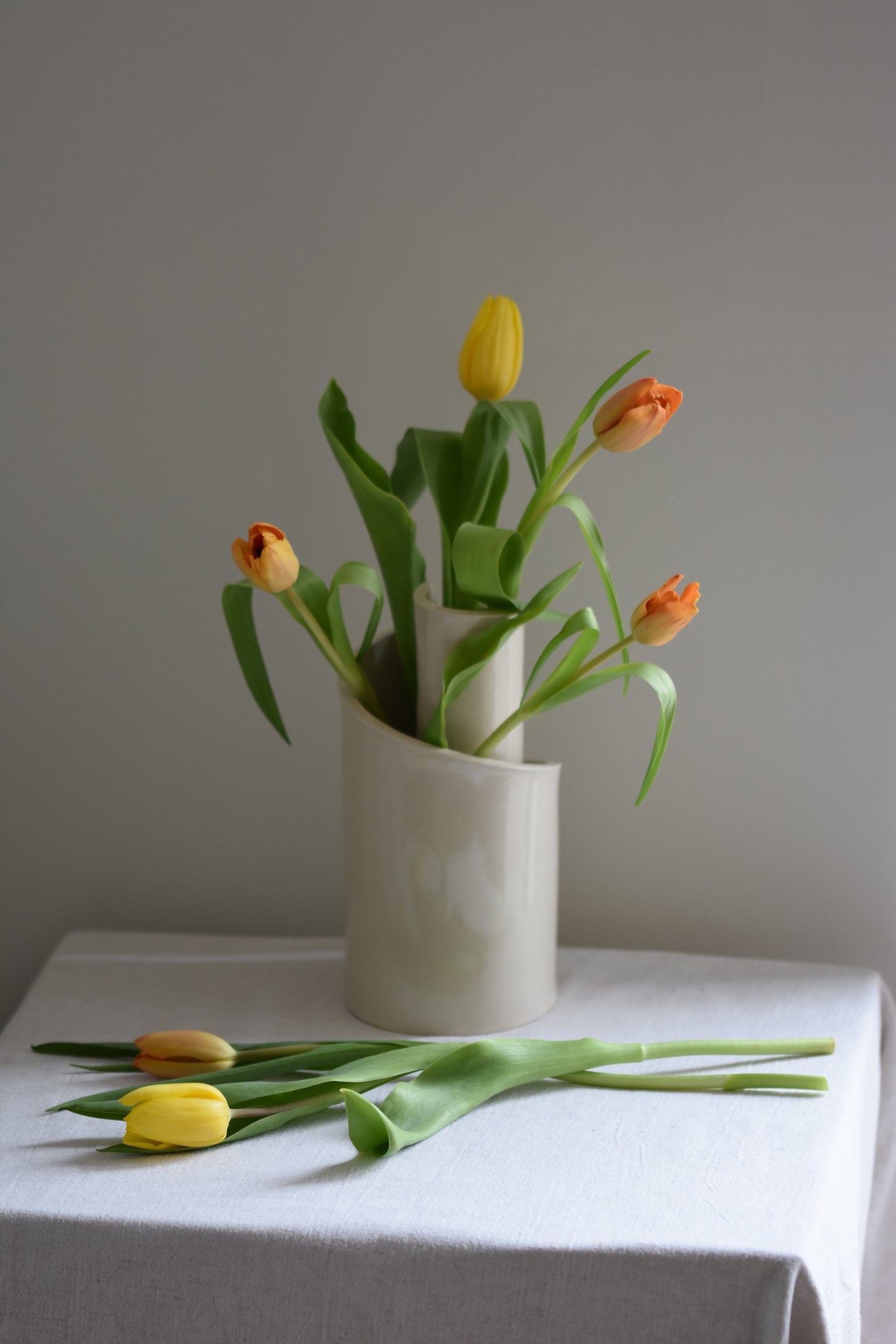 Brutes ceramics cream stoneware vase in a spiral shape with clear glossy finish, filled with orange and yellow tulips.
