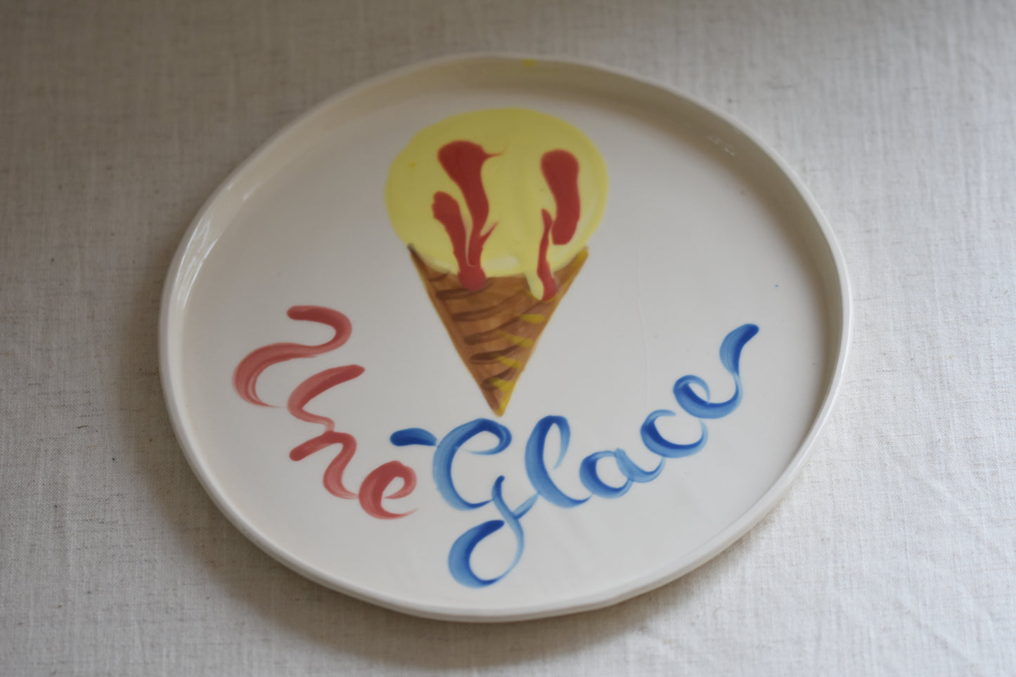 Le Crabe Une Glace ceramic plate with painted ice cream and French writing, on a beige background.