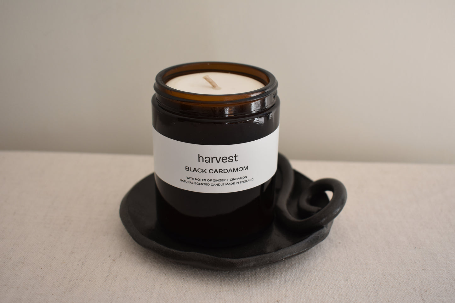 Harvest Black Cardamom candle in brown glass vessel on We Are Clay black ceramic spiral Wee Dish.