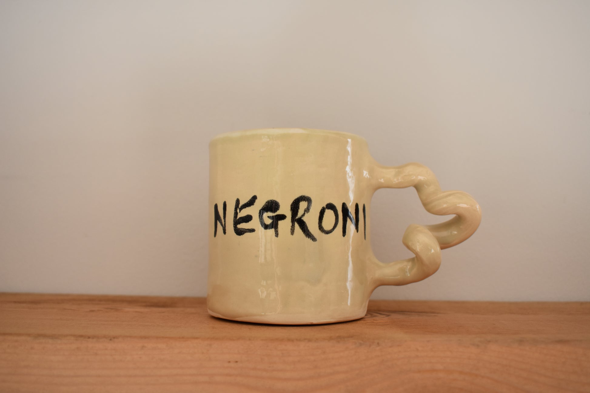 Harlie Brown white earthenware Negroni Wiggle Mug with painted negroni design and writing, and curly handle.