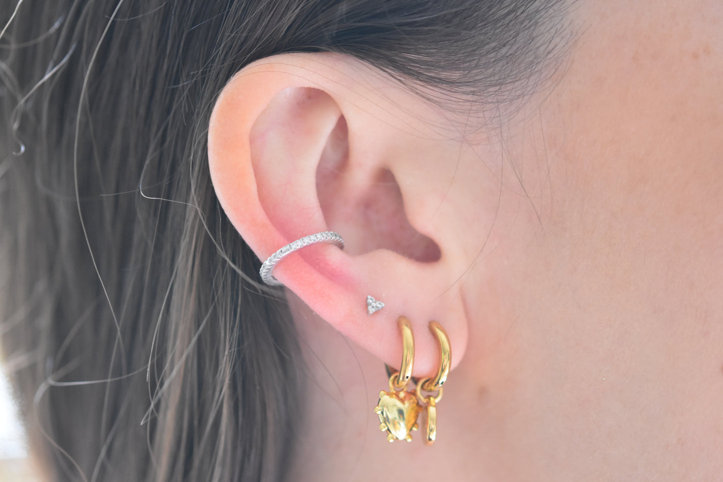 Sandralexandra Mini Milagros Heart hoop earring and Mini Sea Urchin spiral hoop earring in gold worn in a person's ear.