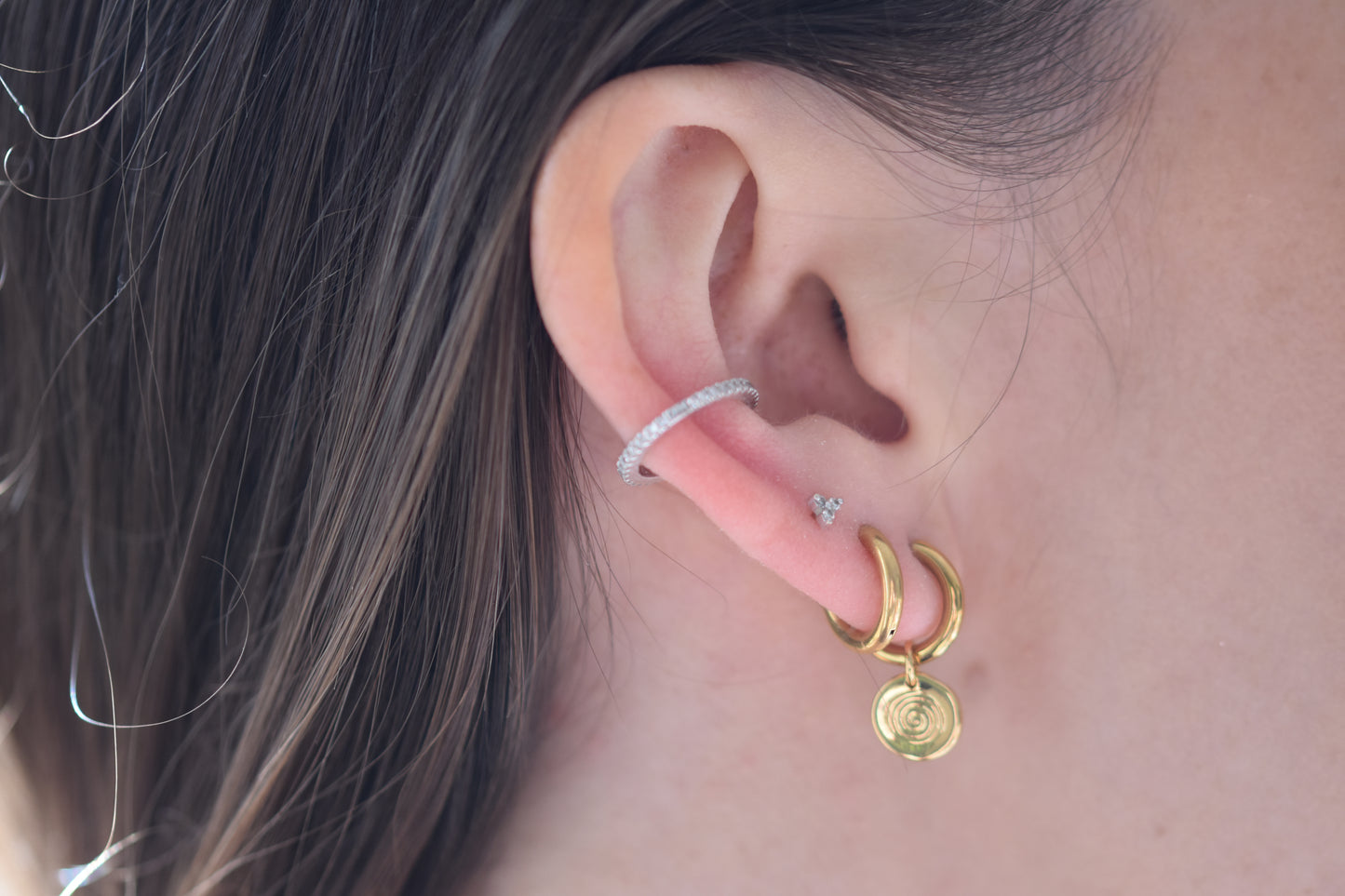 Sandralexandra Mini Sea Urchin spiral hoop earring in gold and gold plain hoop earring worn in a person's ear.