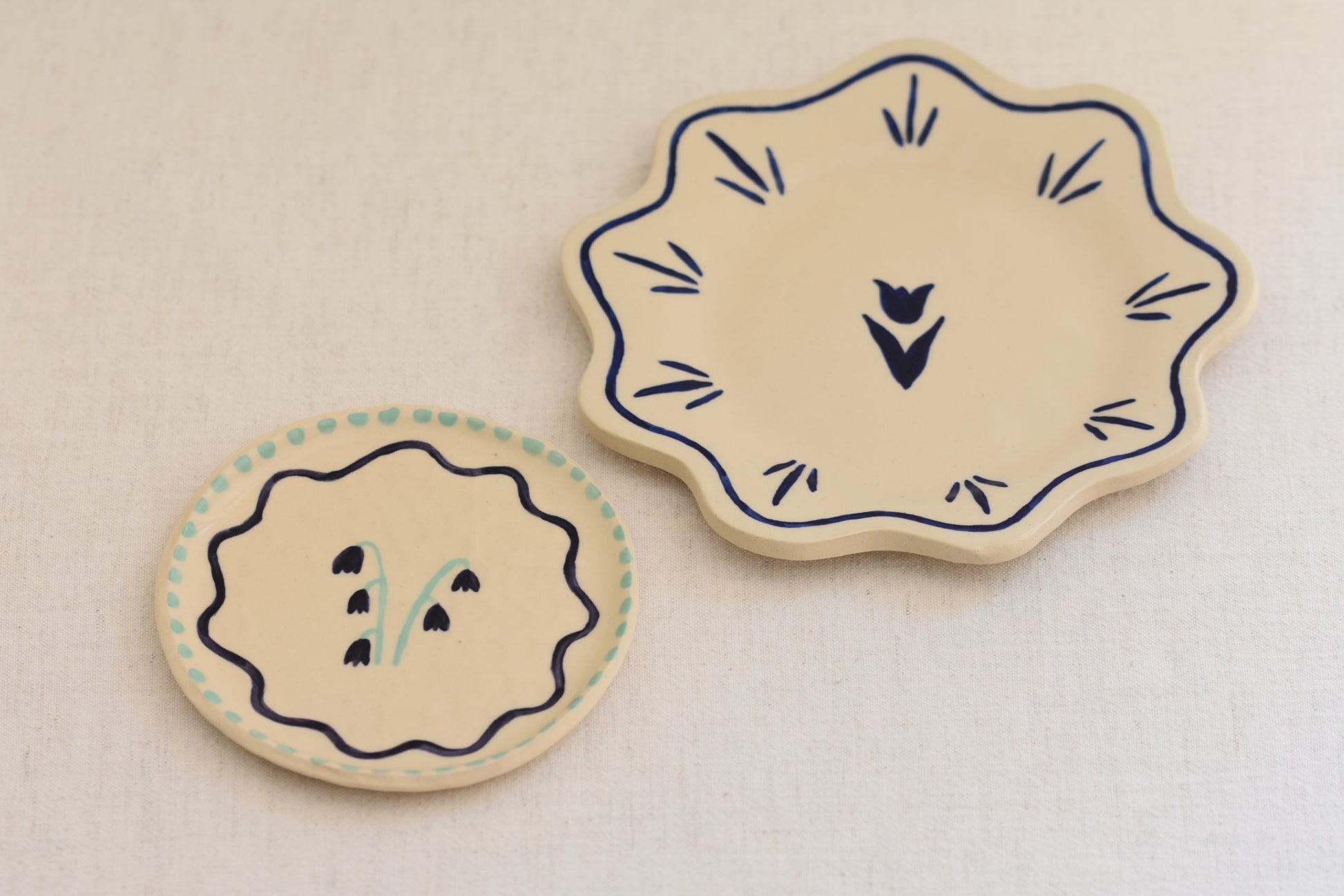Blume Ceramics white stoneware petal shaped plate with hand painted tulip design in navy, and small plate with hand painted bluebell design in navy and green.