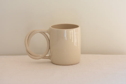 We Are Clay white ceramic mug with pretzel shaped handle on a beige background.