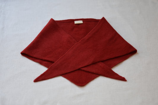 Roake Studio red merino wool triangle scarf folded on a beige background.