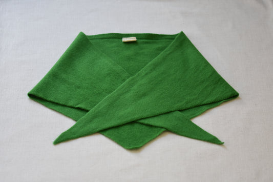 Roake Studio green merino wool triangle scarf folded on a beige background.