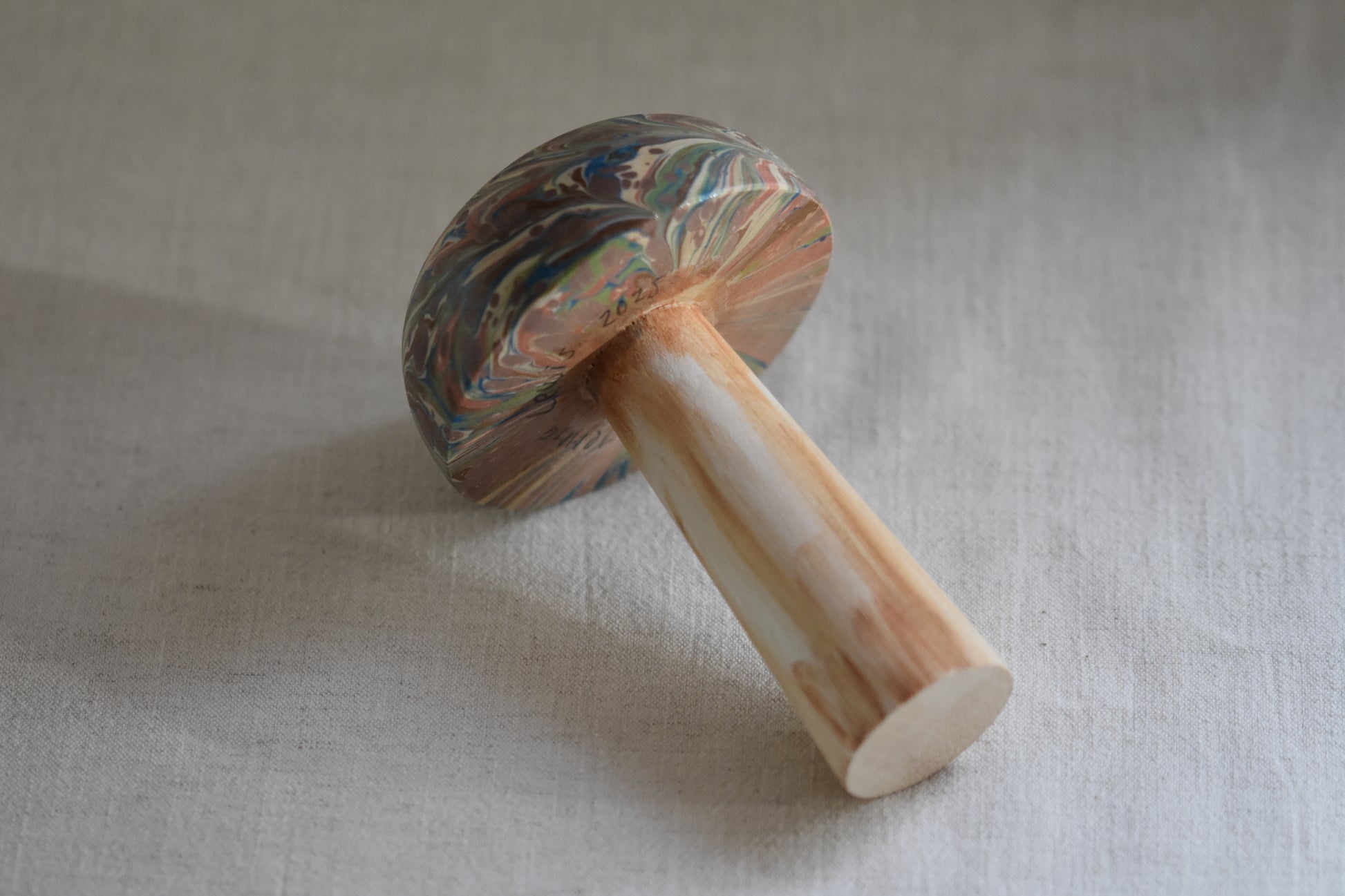 Jemma Lewis marbled wooden decorative toadstool lying down on a beige background.