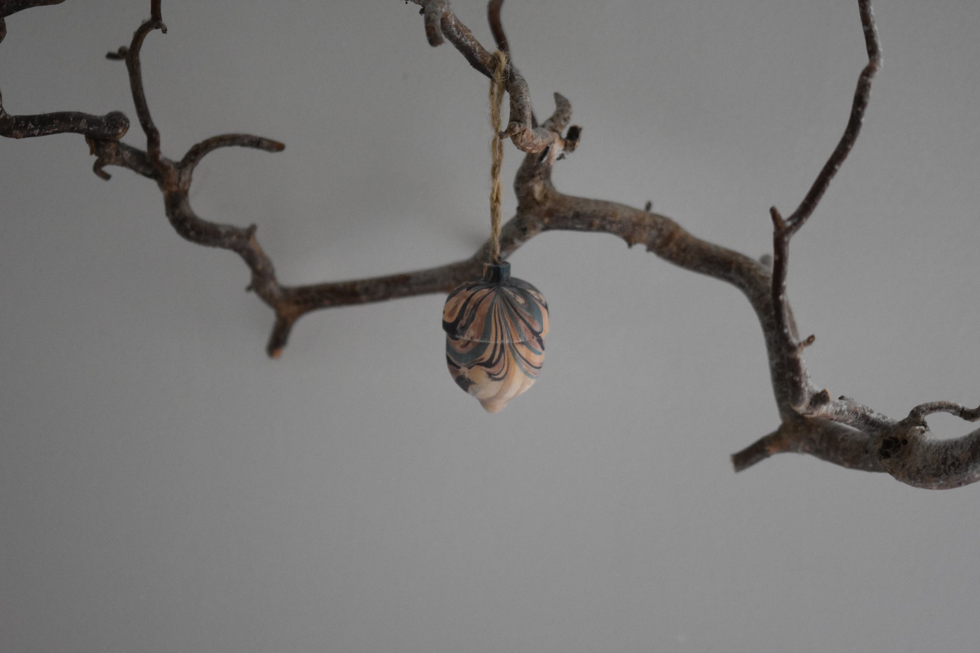 Jemma Lewis marbled wooden decorative acorn hanging from a branch against a white background.