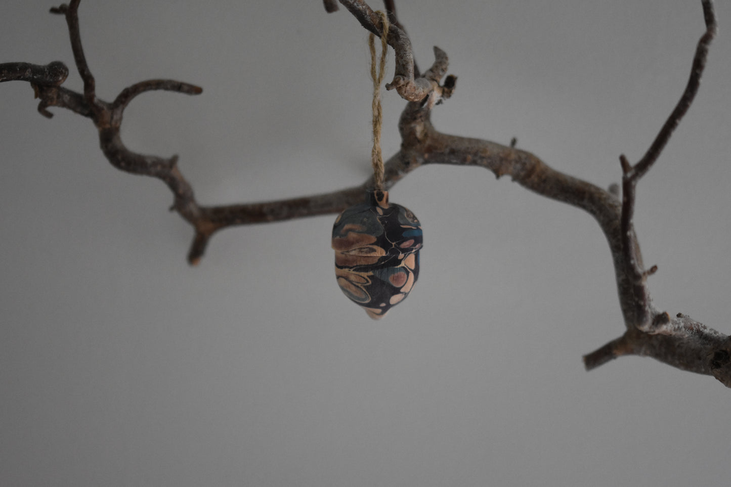 Jemma Lewis marbled wooden decorative acorn hanging from a branch against a white background.