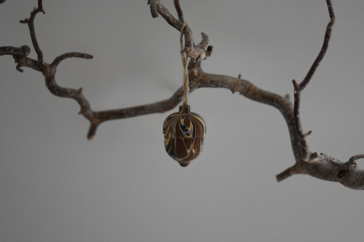 Jemma Lewis marbled wooden decorative acorn hanging from a branch against a white background.