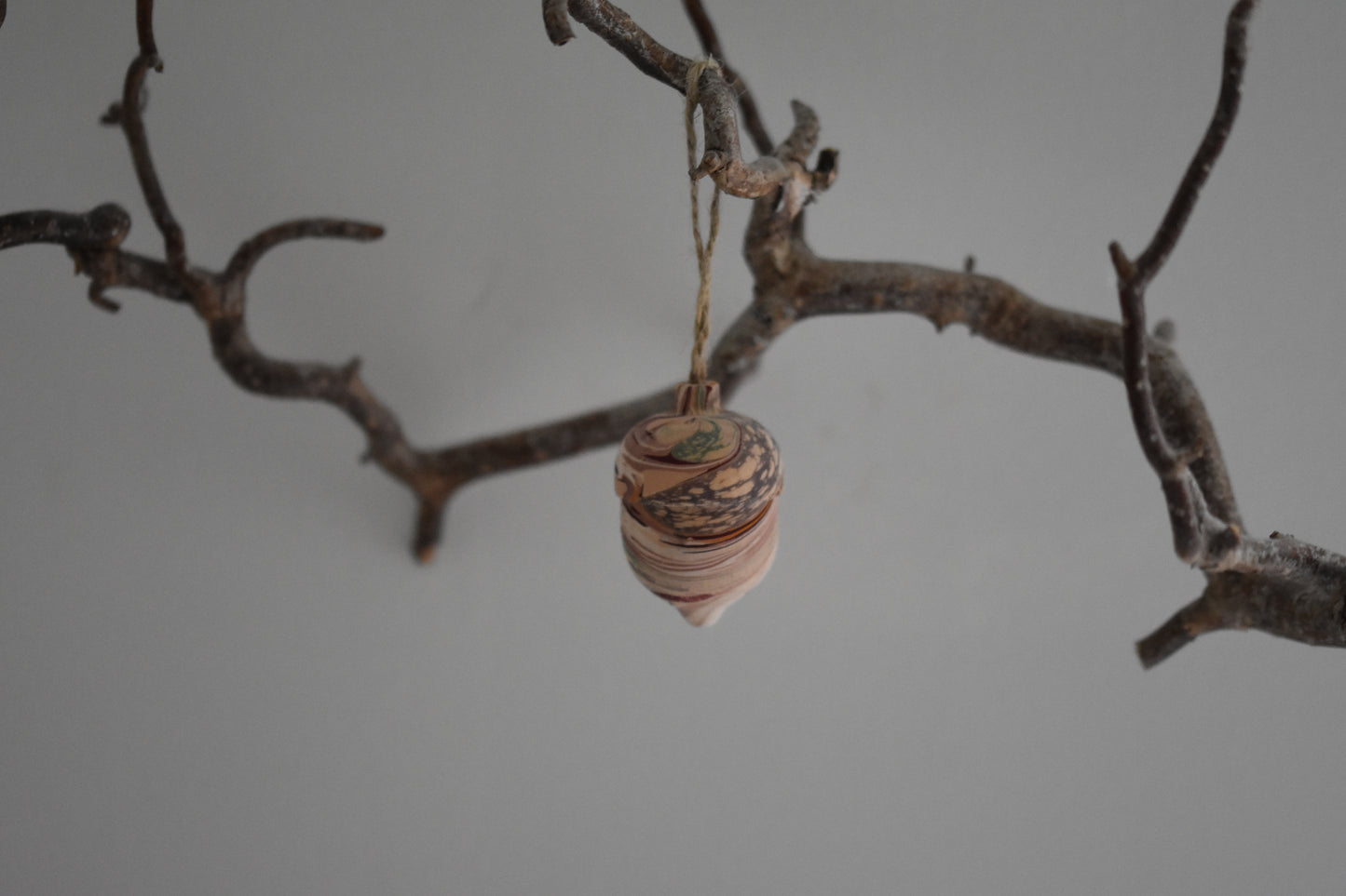 Jemma Lewis marbled wooden decorative acorn hanging from a branch against a white background.
