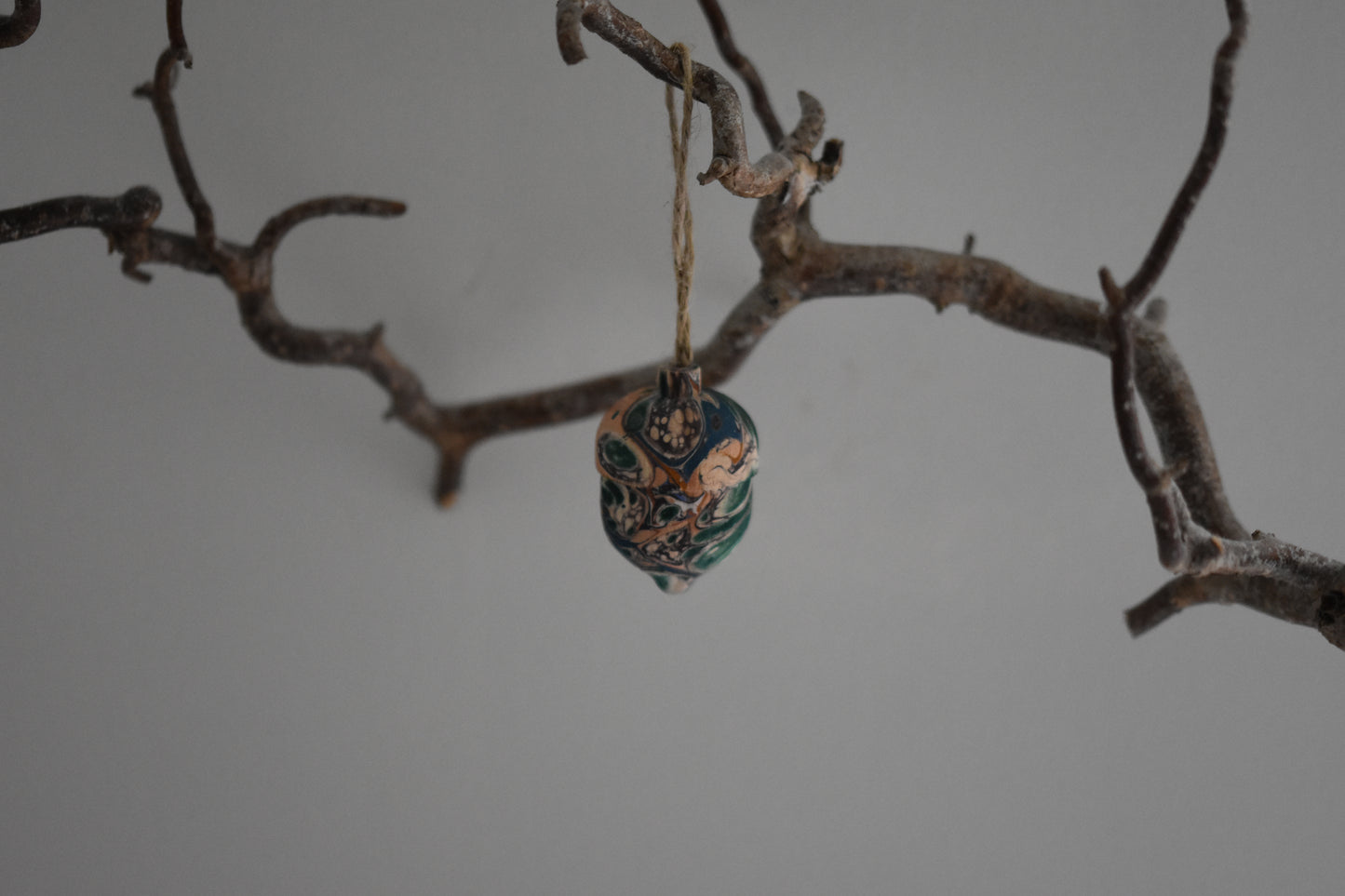Jemma Lewis marbled wooden decorative acorn hanging from a branch against a white background.