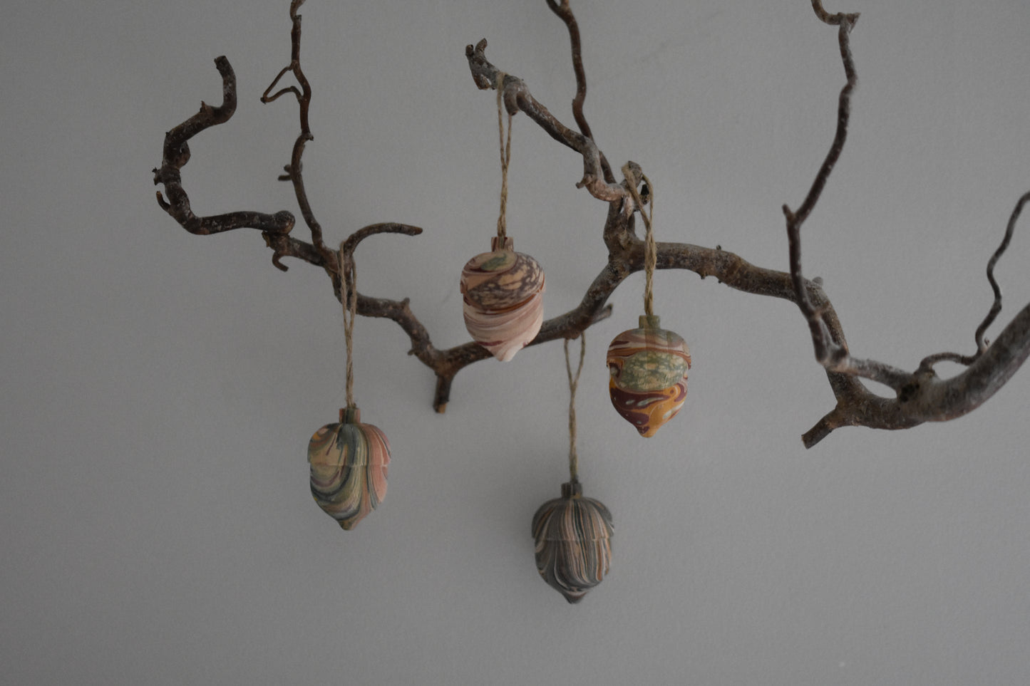 Four Jemma Lewis marbled wooden decorative acorns hanging from a branch against a white background.