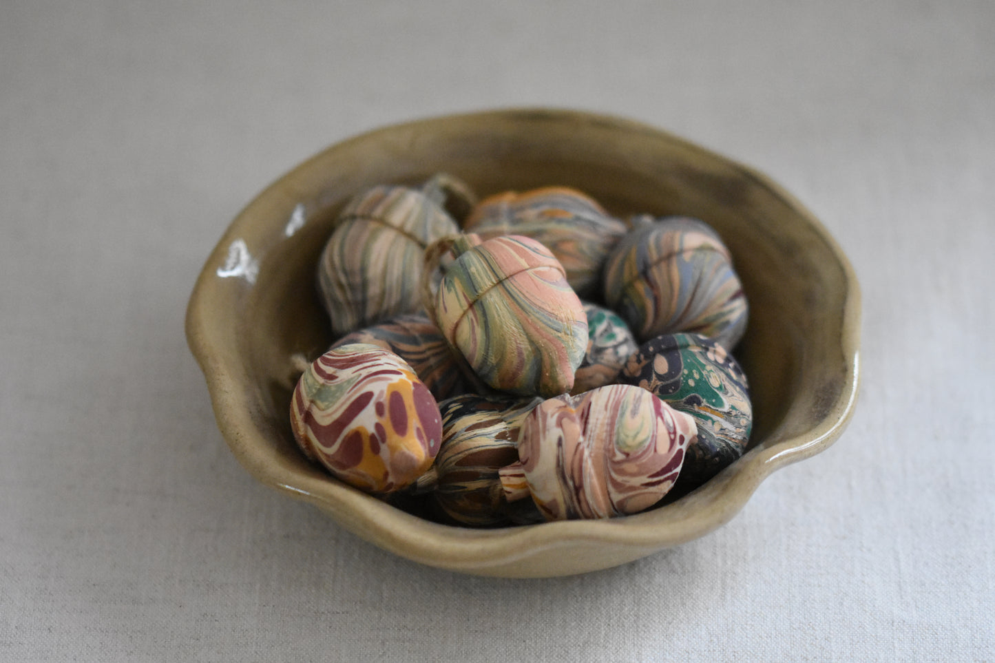 Jemma Lewis marbled decorative wooden acorns in a beige ceramic wavy bowl on a cream background.