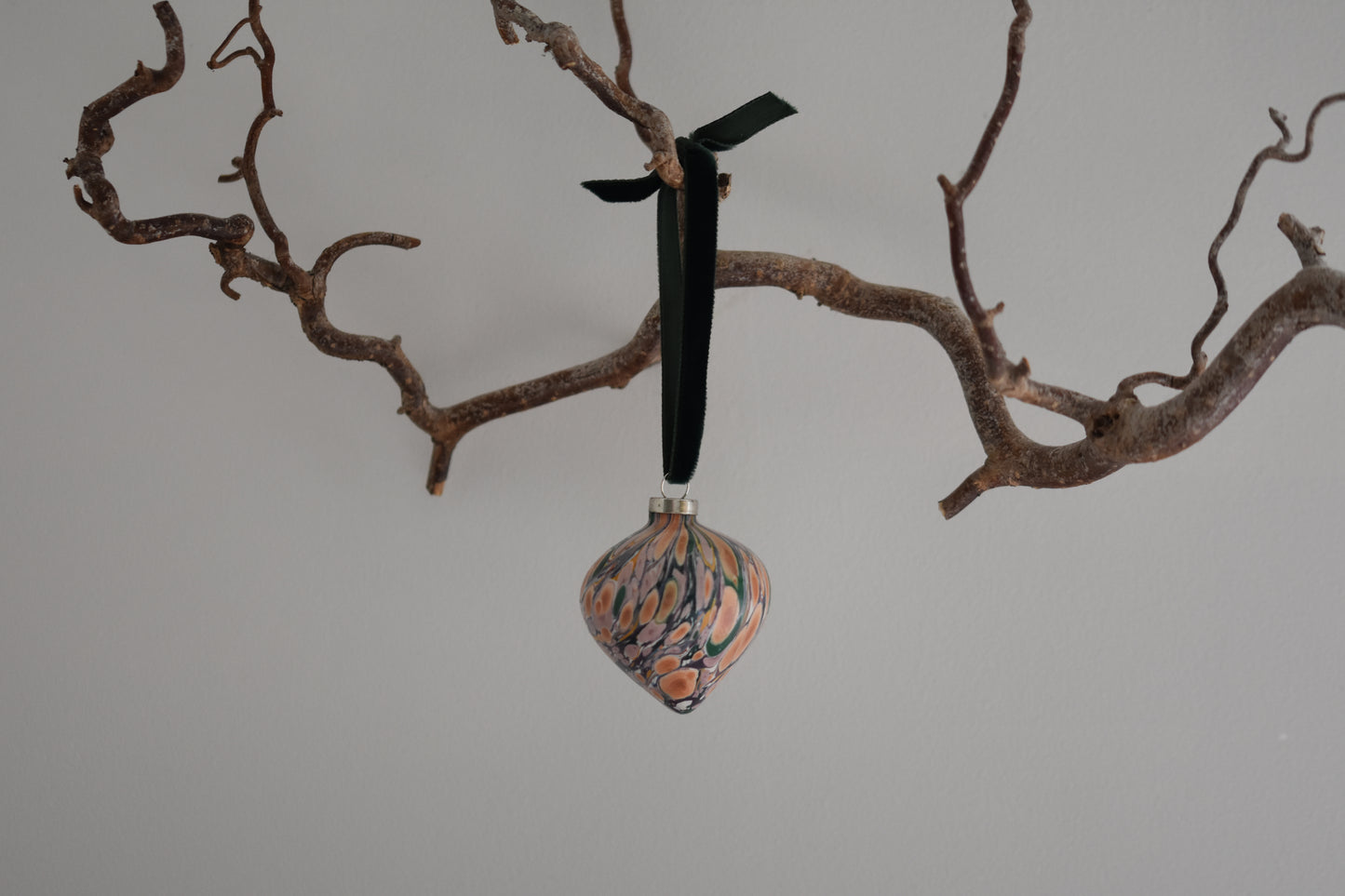 Jemma Lewis colourful marbled teardrop ceramic bauble Christmas ornament with velvet ribbon, hanging from a branch on a white background.