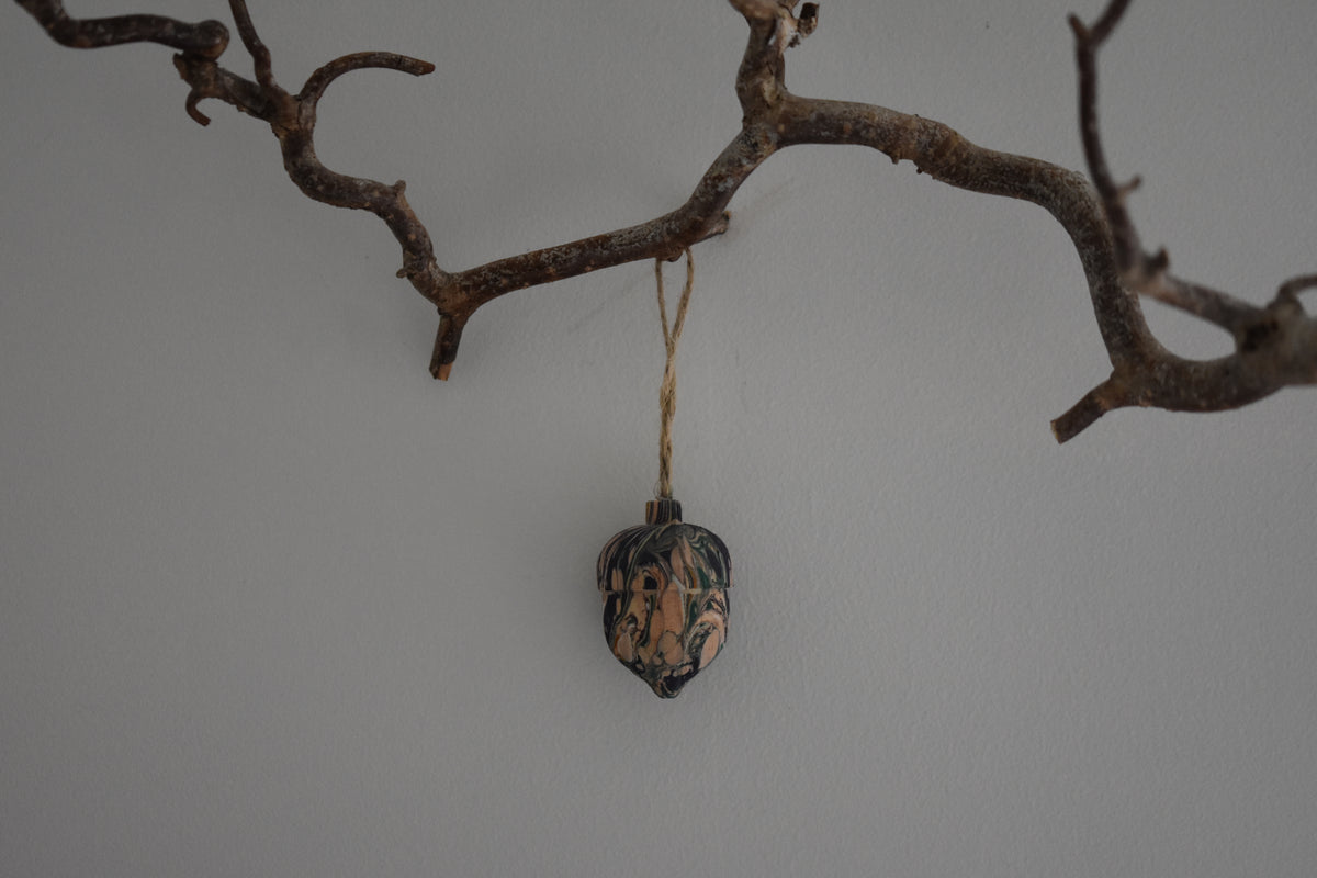 Jemma Lewis colourful marbled wooden acorn decoration Christmas ornament hung from twine on a branch, with a white background.