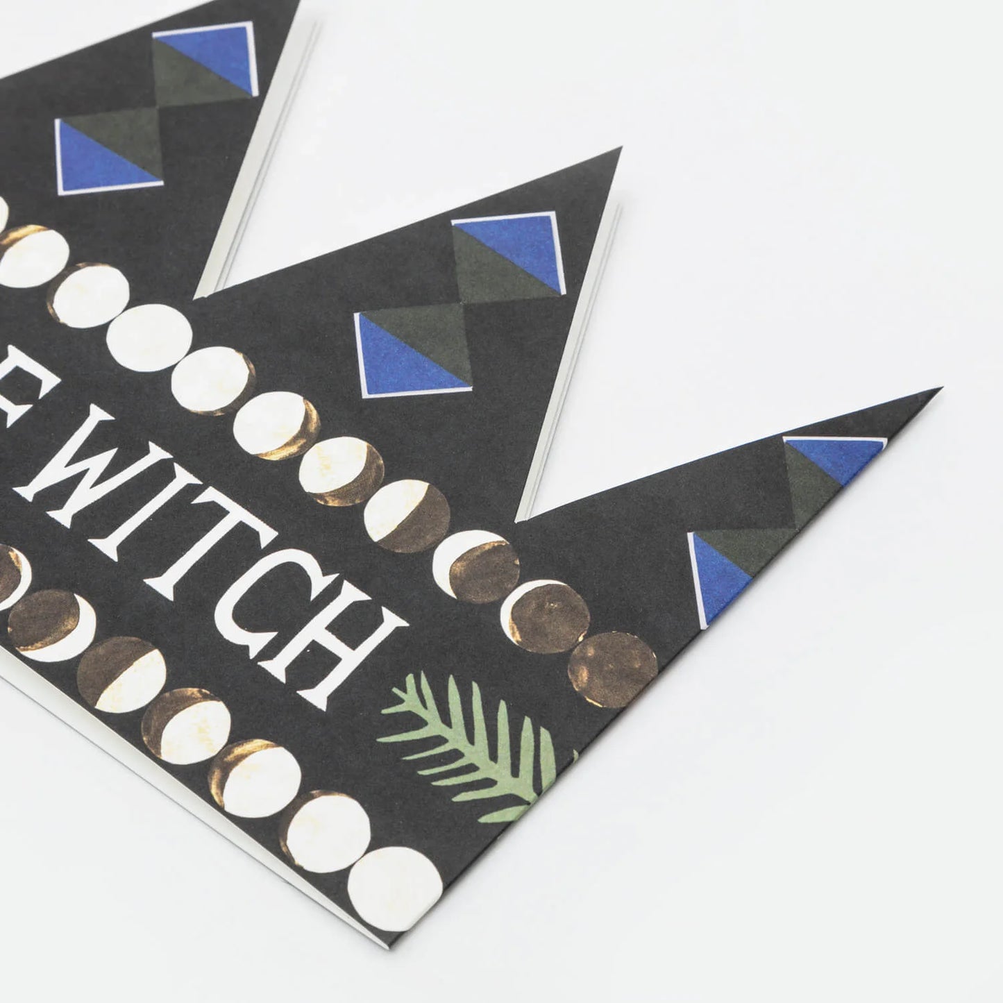 Hadley Paper Goods Chief Witch party hat crown shaped card in black with blue, green and white pattern, close up, on a white background.