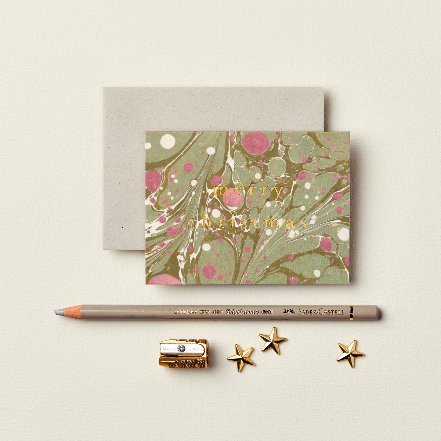 Wanderlust Paper Co. mini green and red marble card with Merry Christmas in gold, shown next to stationery on a pale grey background.