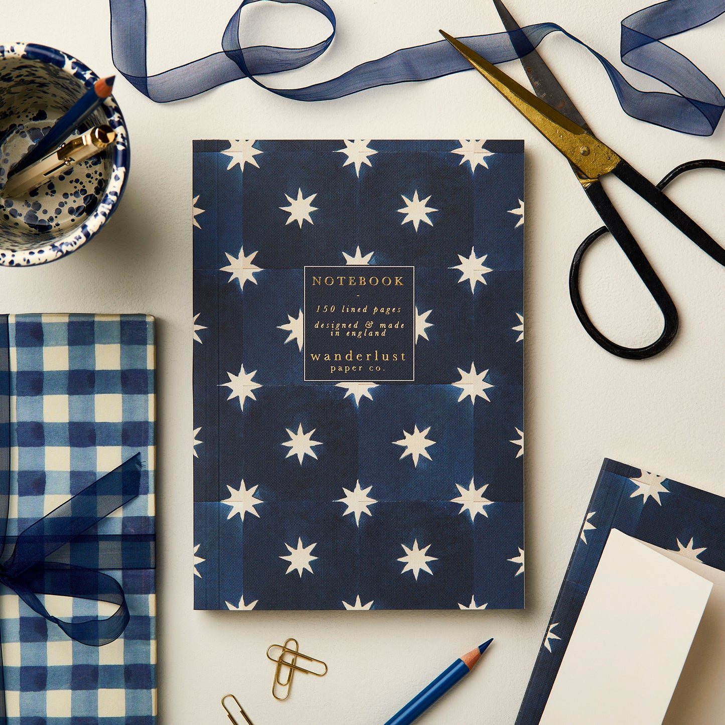 Wanderlust Paper Co. navy with white star print notebook, surrounded by stationery, on a light grey background.