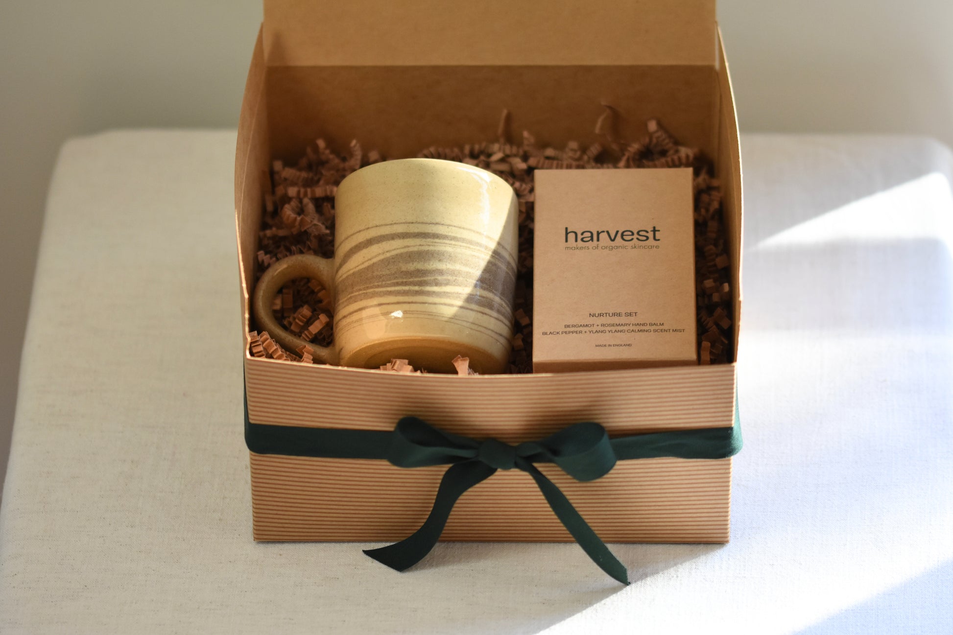 RORA kraft gift box with green ribbon containing a Ceramics by Sunny marble mug and Harvest nurture set, on a beige background.