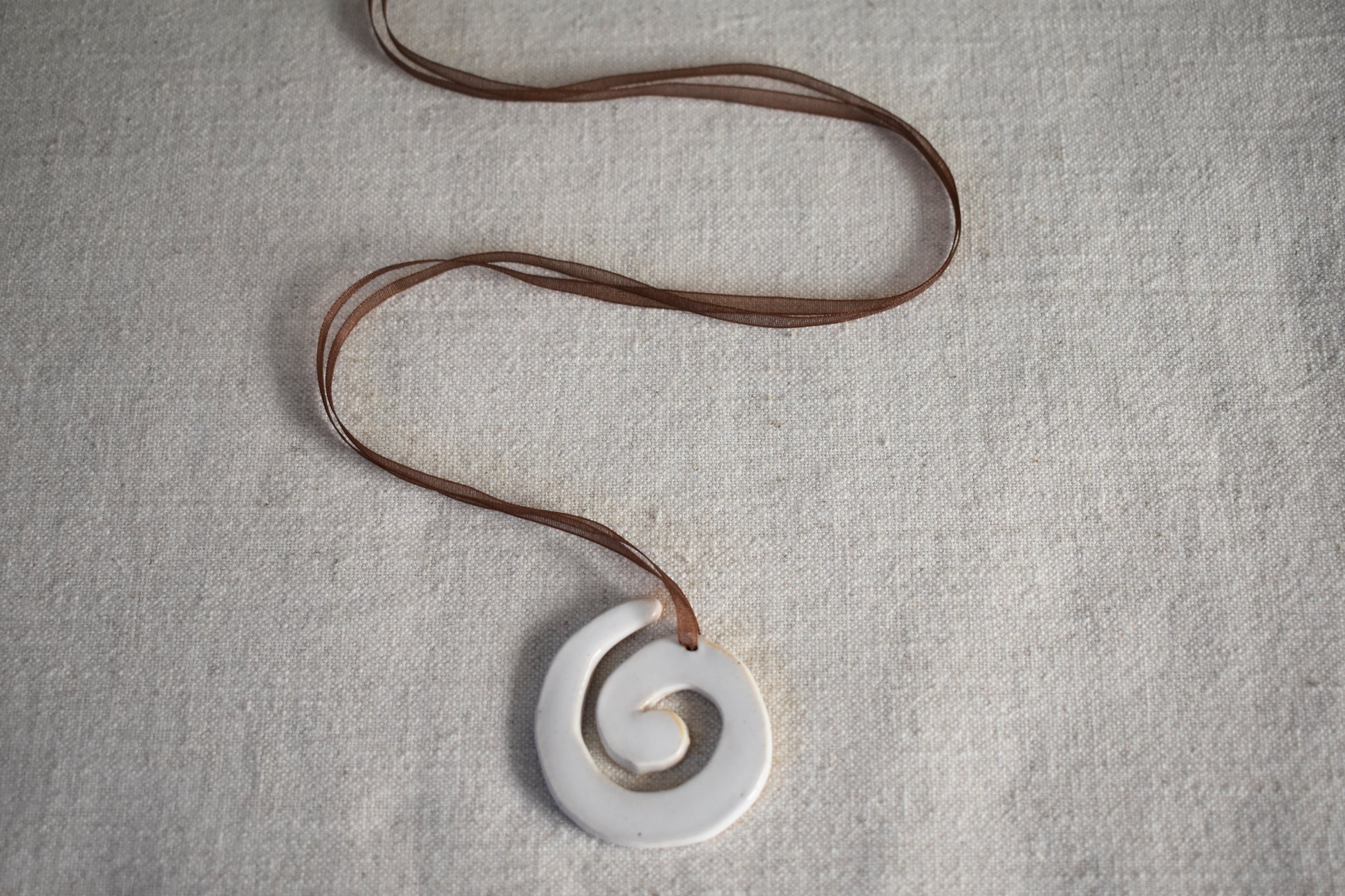 AEA Studio white mini stoneware ceramic swirl spiral pendant on a brown ribbon necklace.