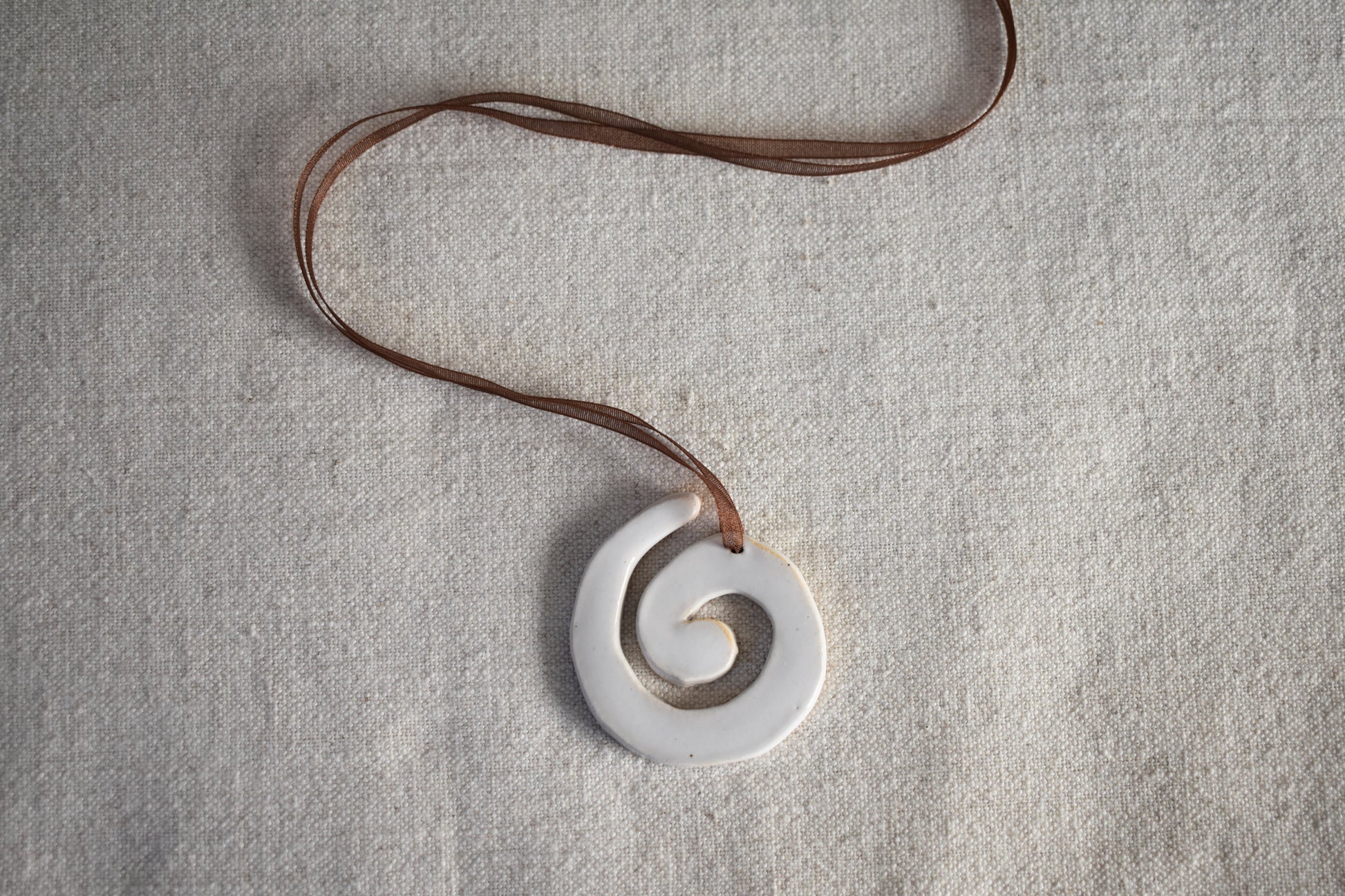 AEA Studio white mini stoneware ceramic swirl spiral pendant on a brown ribbon necklace.