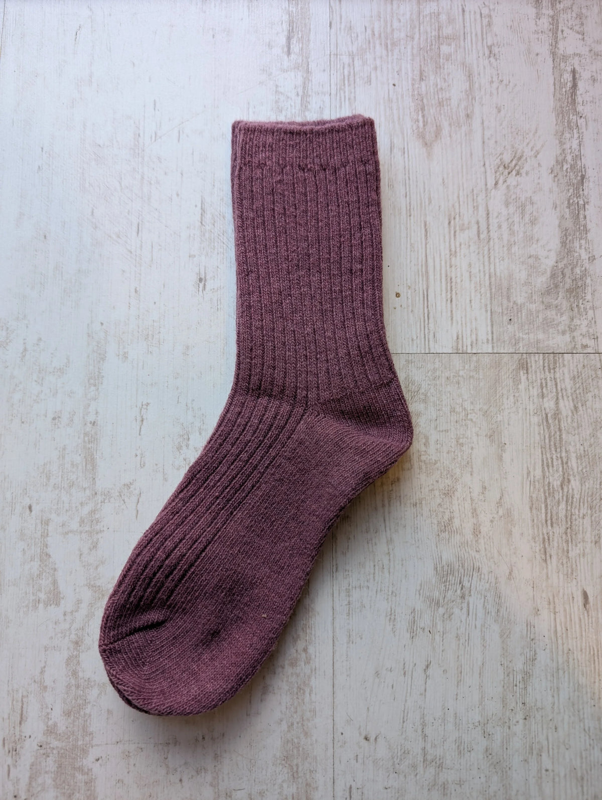 A pair of maroon purple ribbed knit Merino wool socks laid flat on a light wood surface.