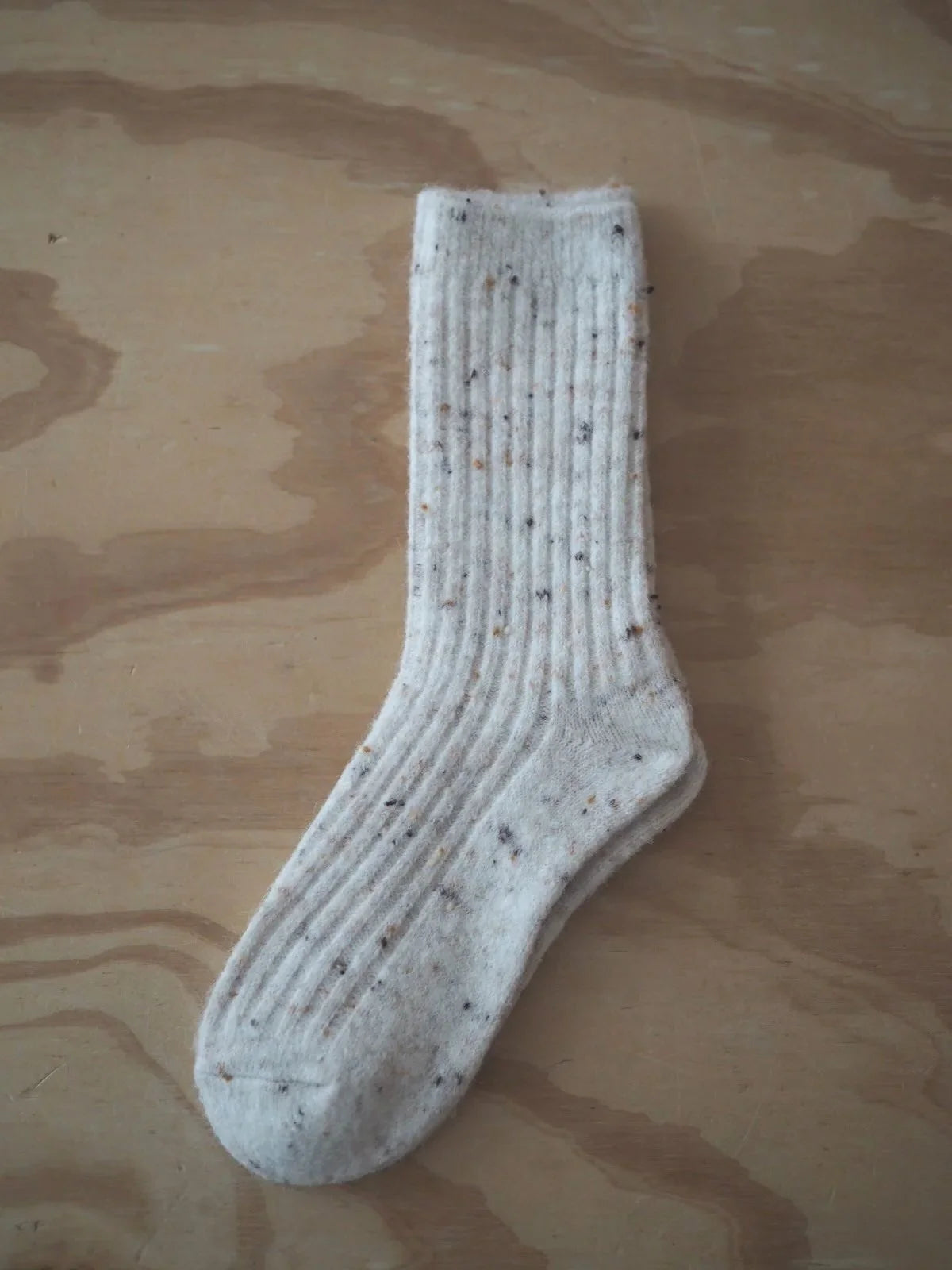 A pair of beige fleck ribbed knit Merino wool socks laid flat on a light wood surface.