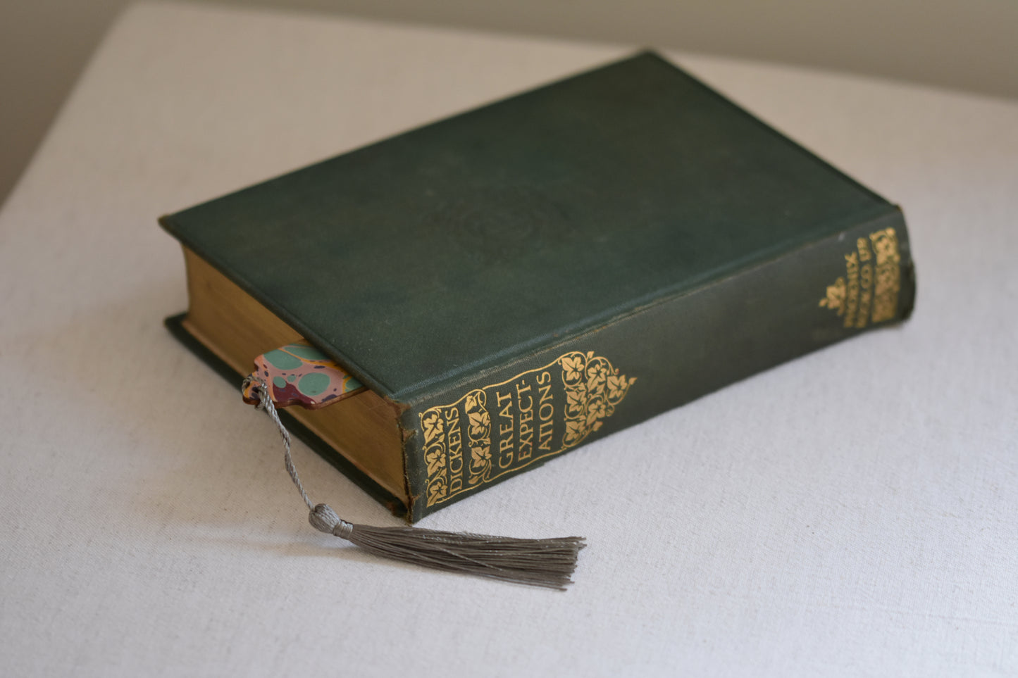 Jemma Lewis marbled bookmark with grey tassel in a vintage green and gold book, on a beige background.